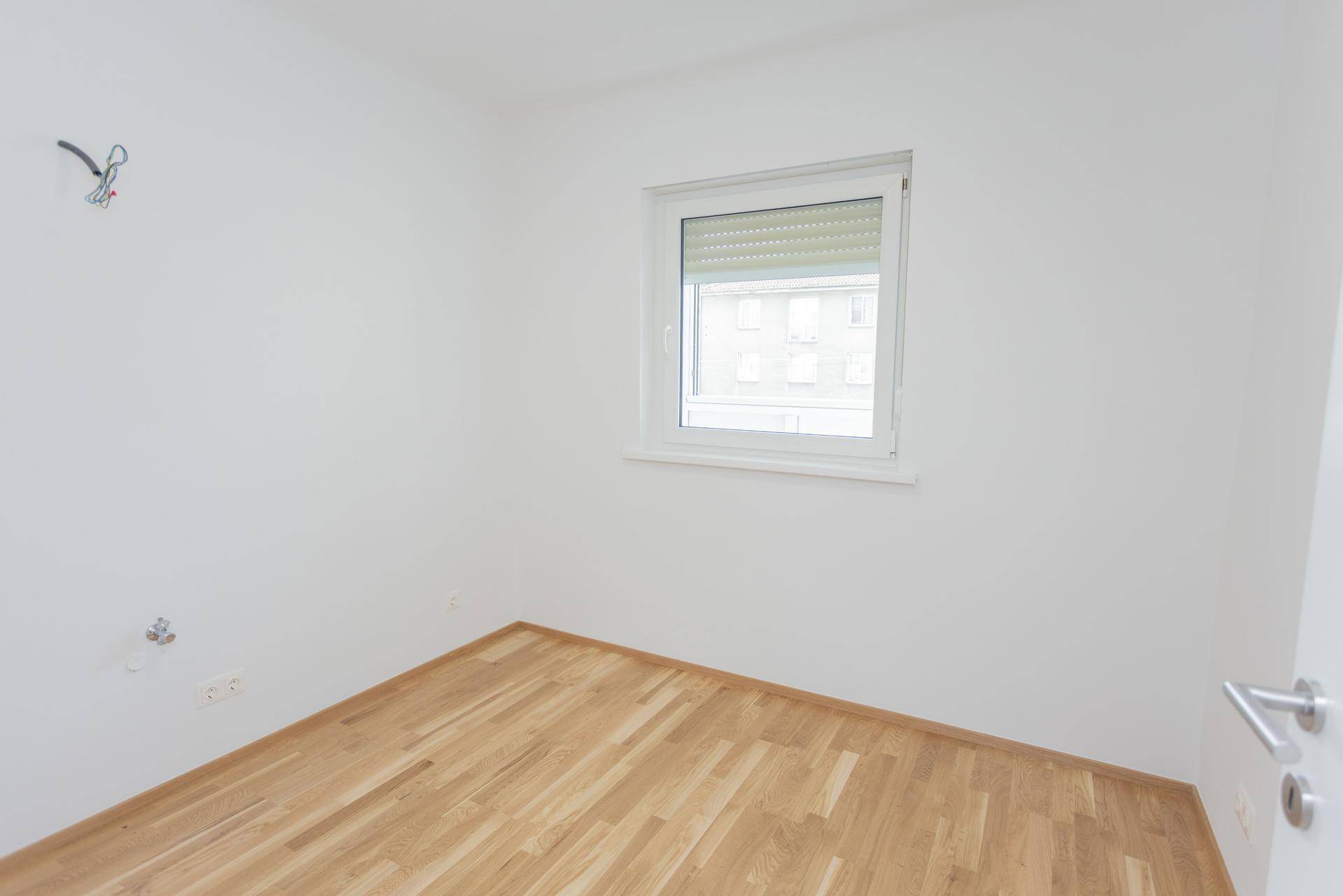 Leerer Raum mit Holzboden und Fenster, vorbereitet für die Installation einer Küche.