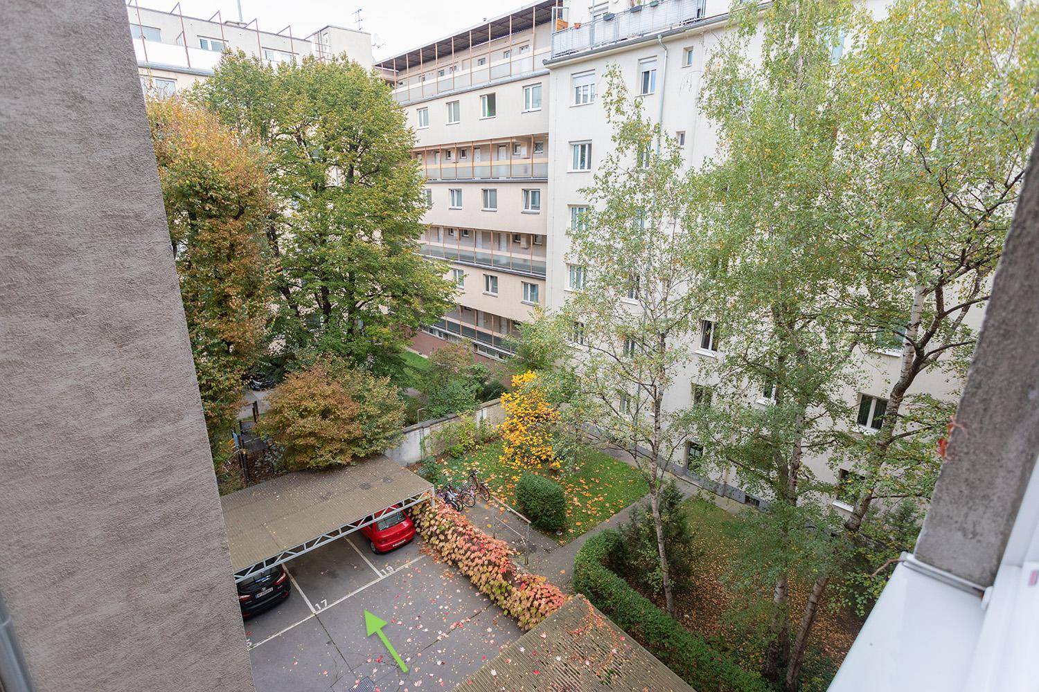 Außenansicht mit überdachtem Parkplatz und umliegenden Wohngebäuden im Grünen.