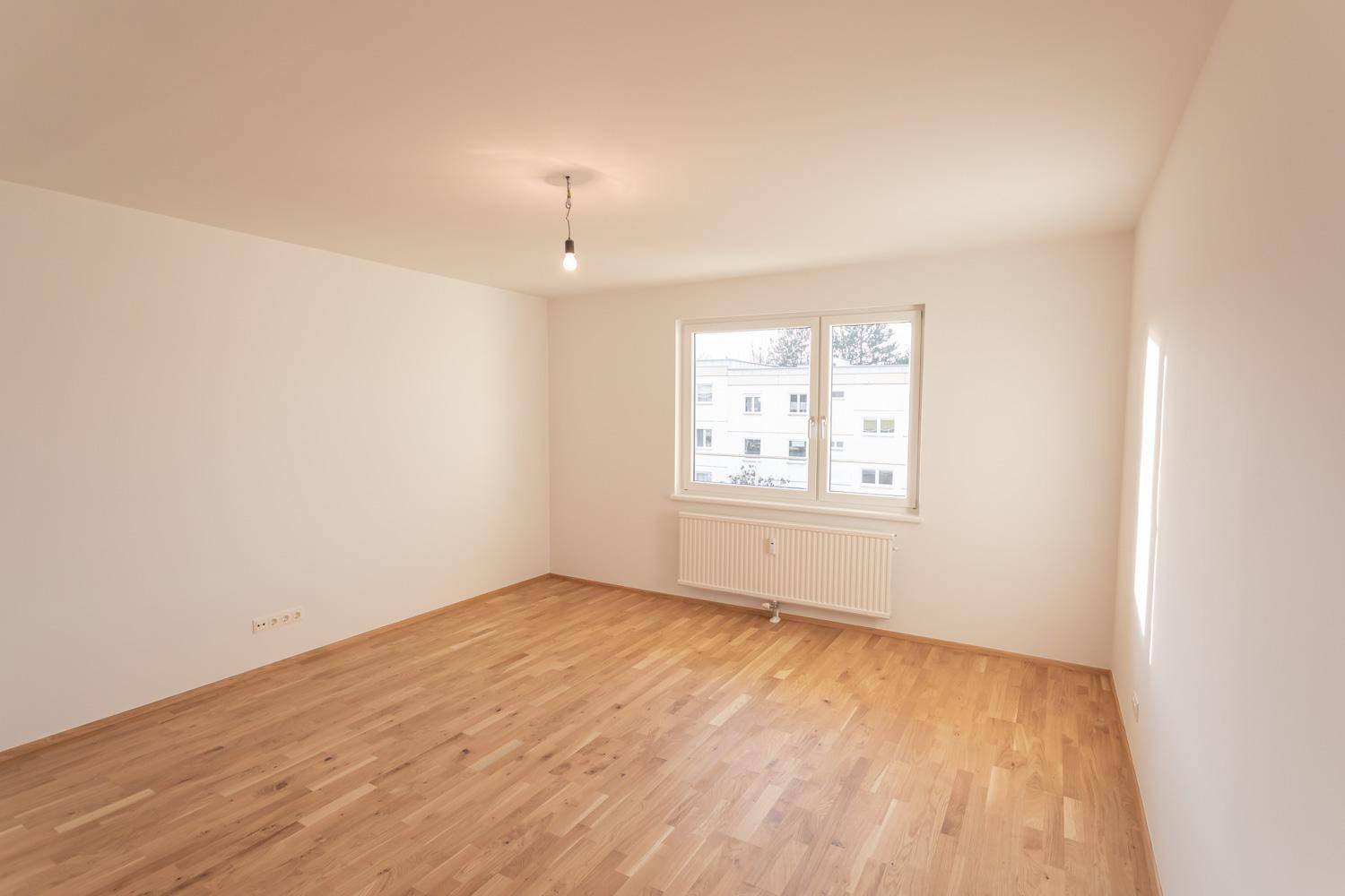 Lichtdurchflutetes, leeres Zimmer mit Parkettboden und breitem Fenster.