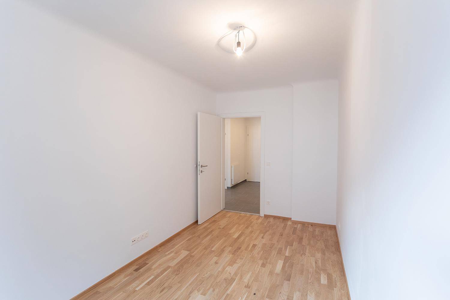 Leeres Zimmer mit Parkettboden und Zugang zum gefliesten Flur.