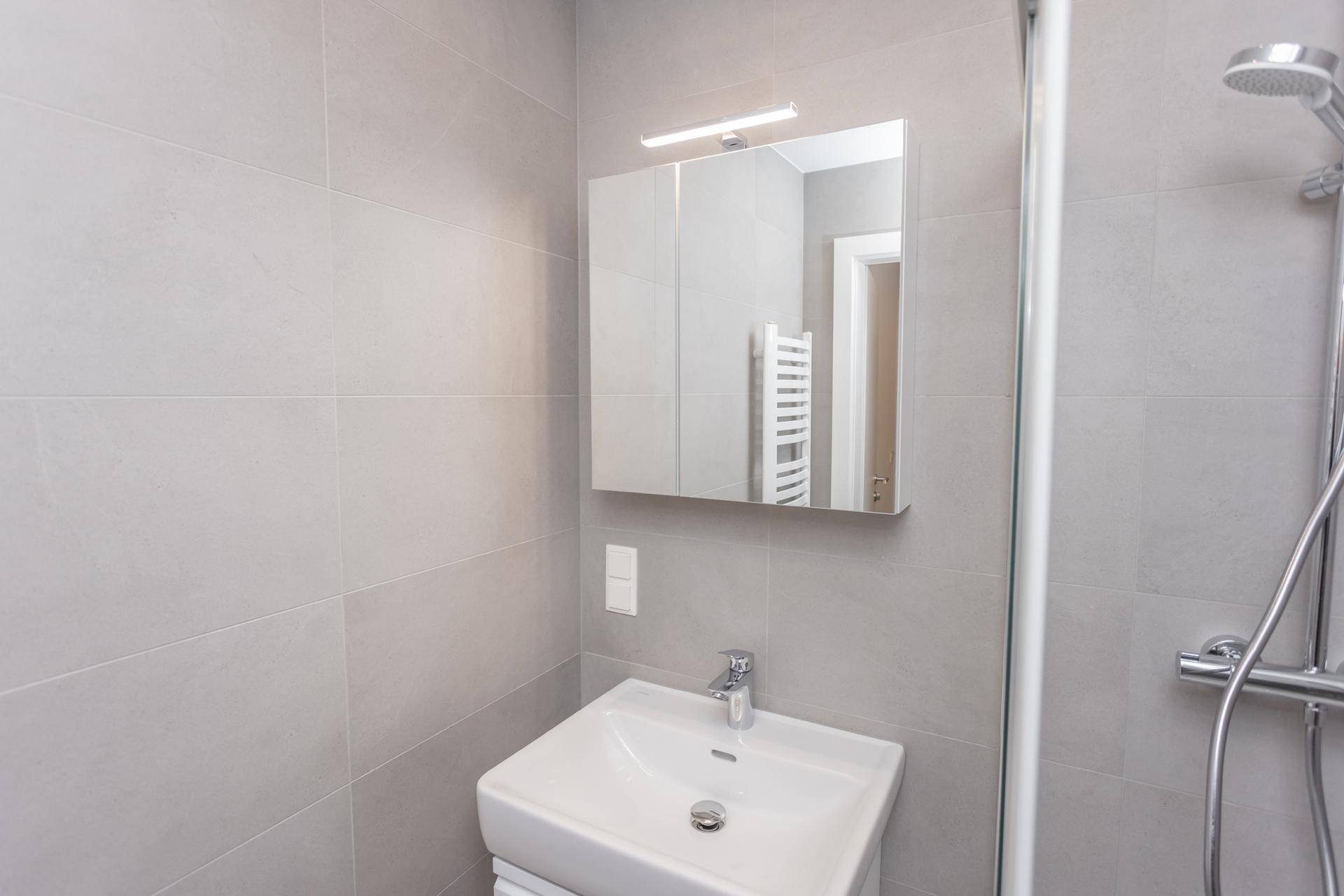 Detailansicht des modernen Badezimmers mit Waschtisch, Spiegelschrank und Duschbereich.