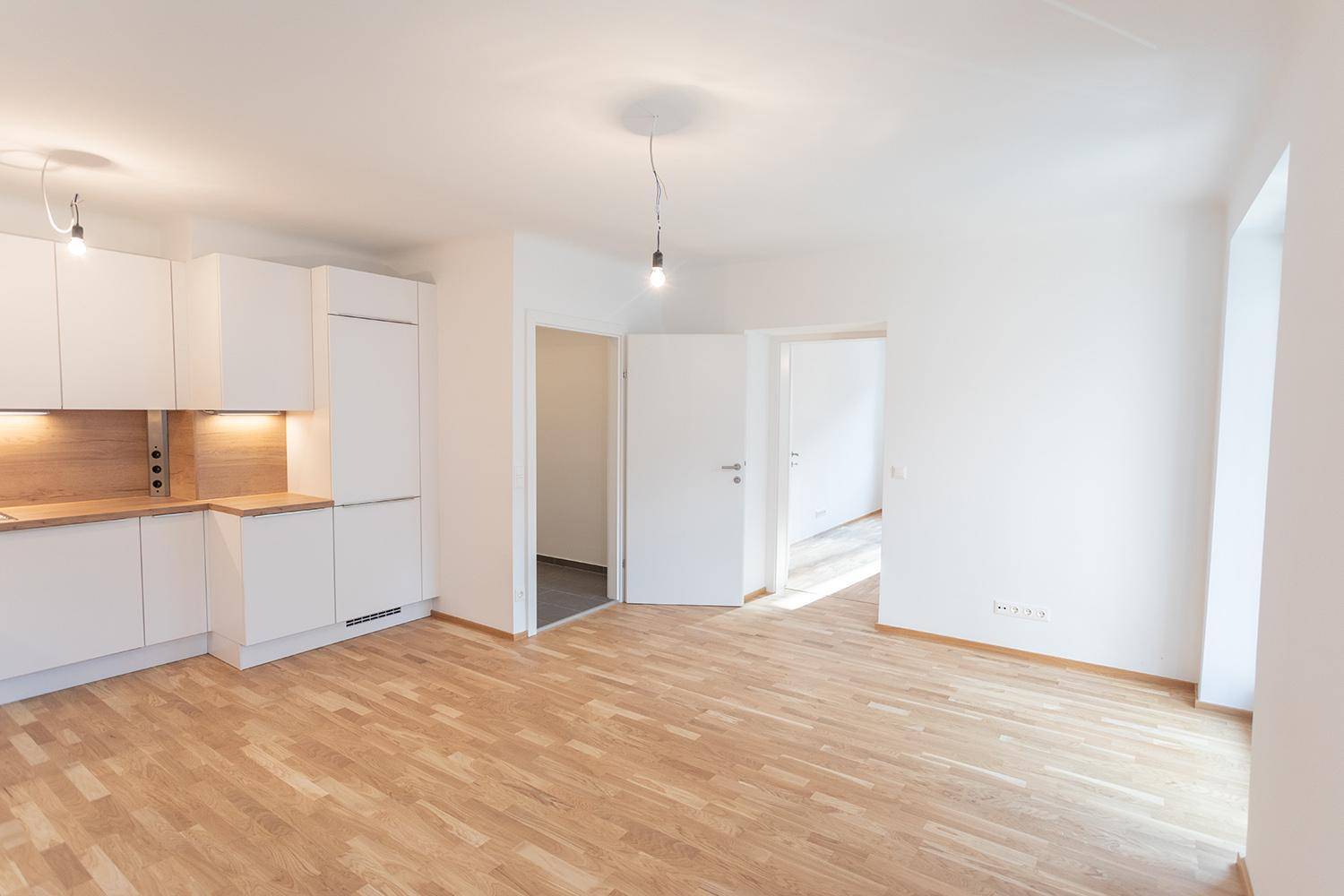 Geräumige Küche mit weißen Schränken, Holzarbeitsplatten und Zugang zum Flur.