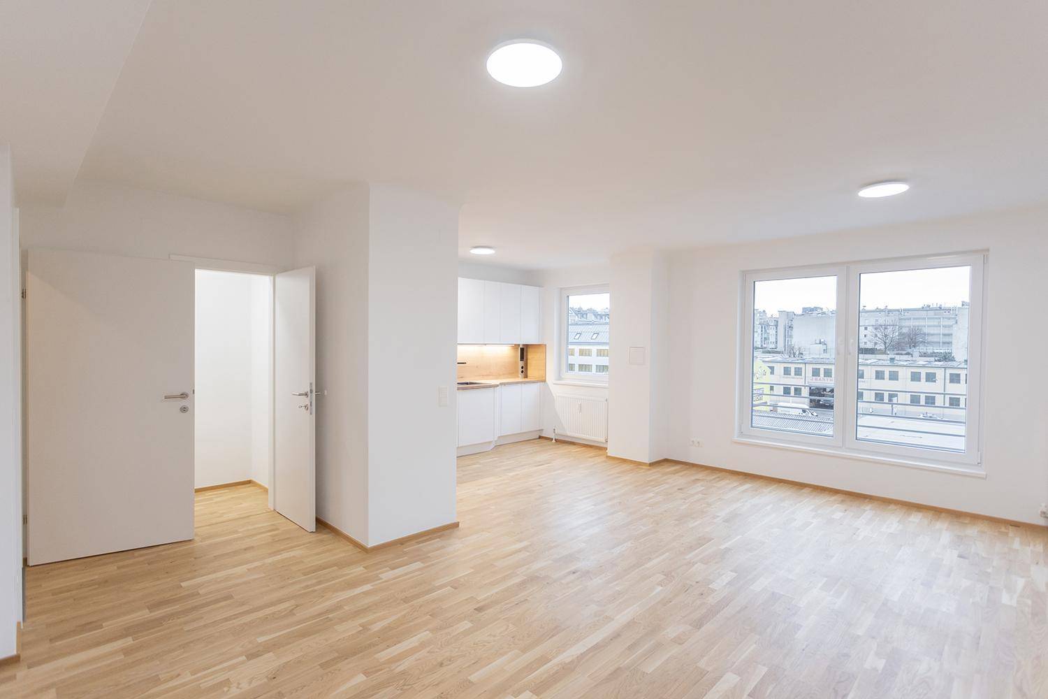 Offener Wohnbereich mit moderner Einbauküche und hellem Holzboden.