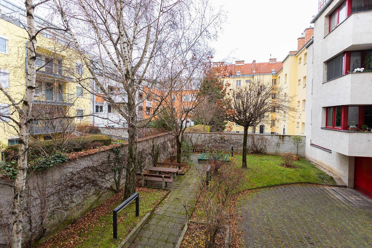 Grüner Innenhof mit Bäumen, Sitzgelegenheiten und gepflasterten Wegen zwischen den Wohngebäuden.