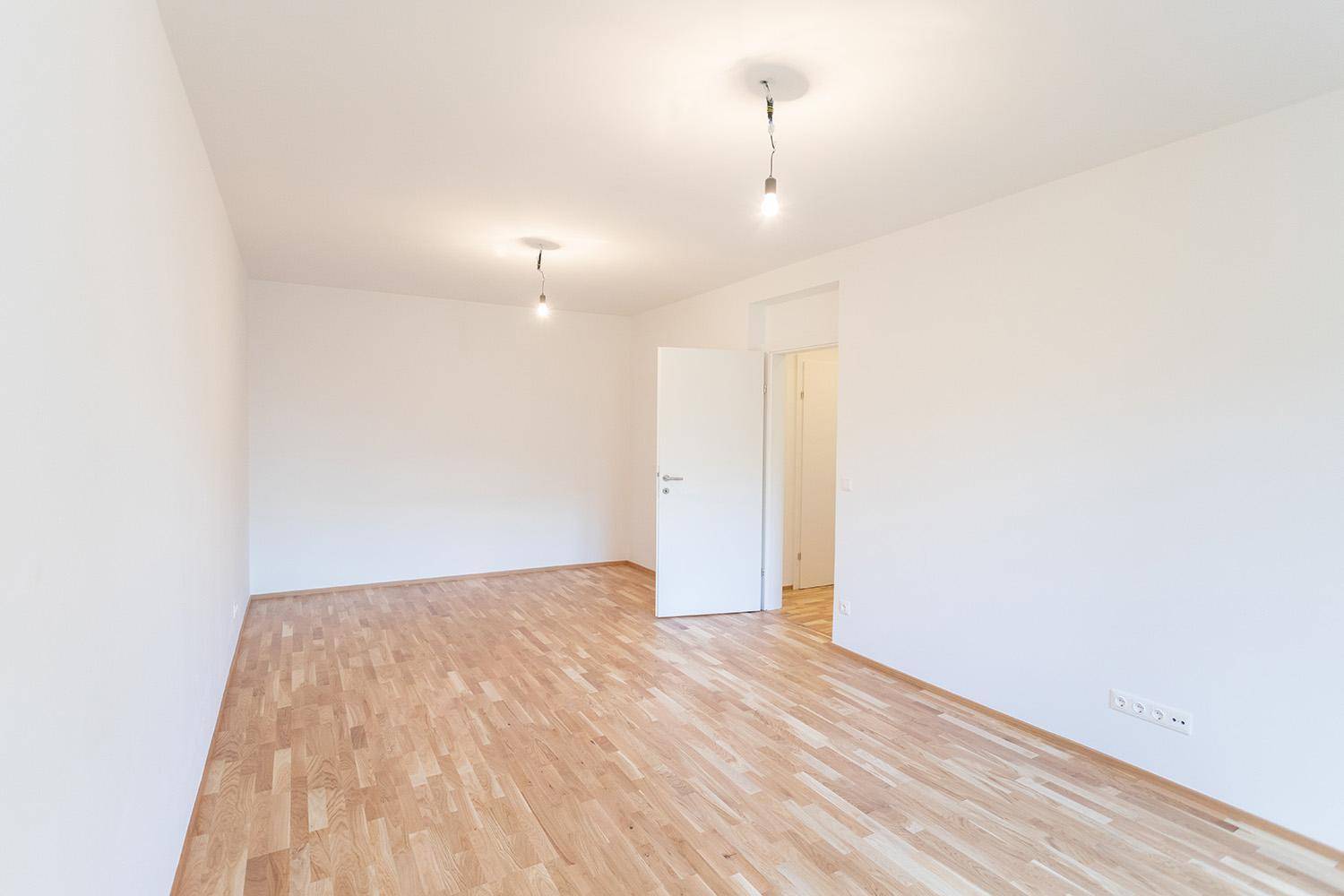 Leeres Zimmer mit Holzboden und weiß gestrichenen Wänden, ideal für individuelle Gestaltung.