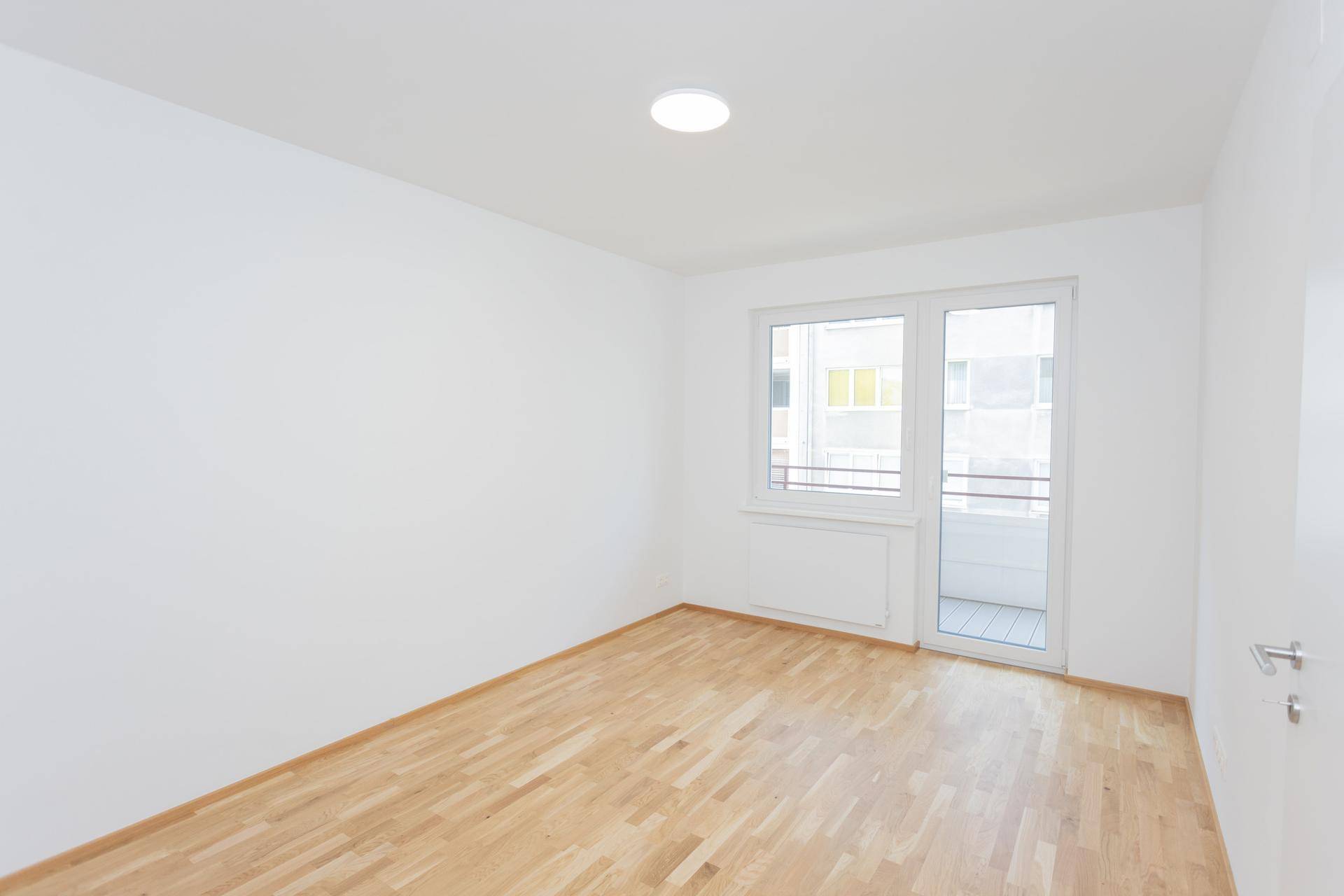 Helles Schlafzimmer mit Parkettboden und direktem Zugang zu einem Balkon, bietet viel Licht.