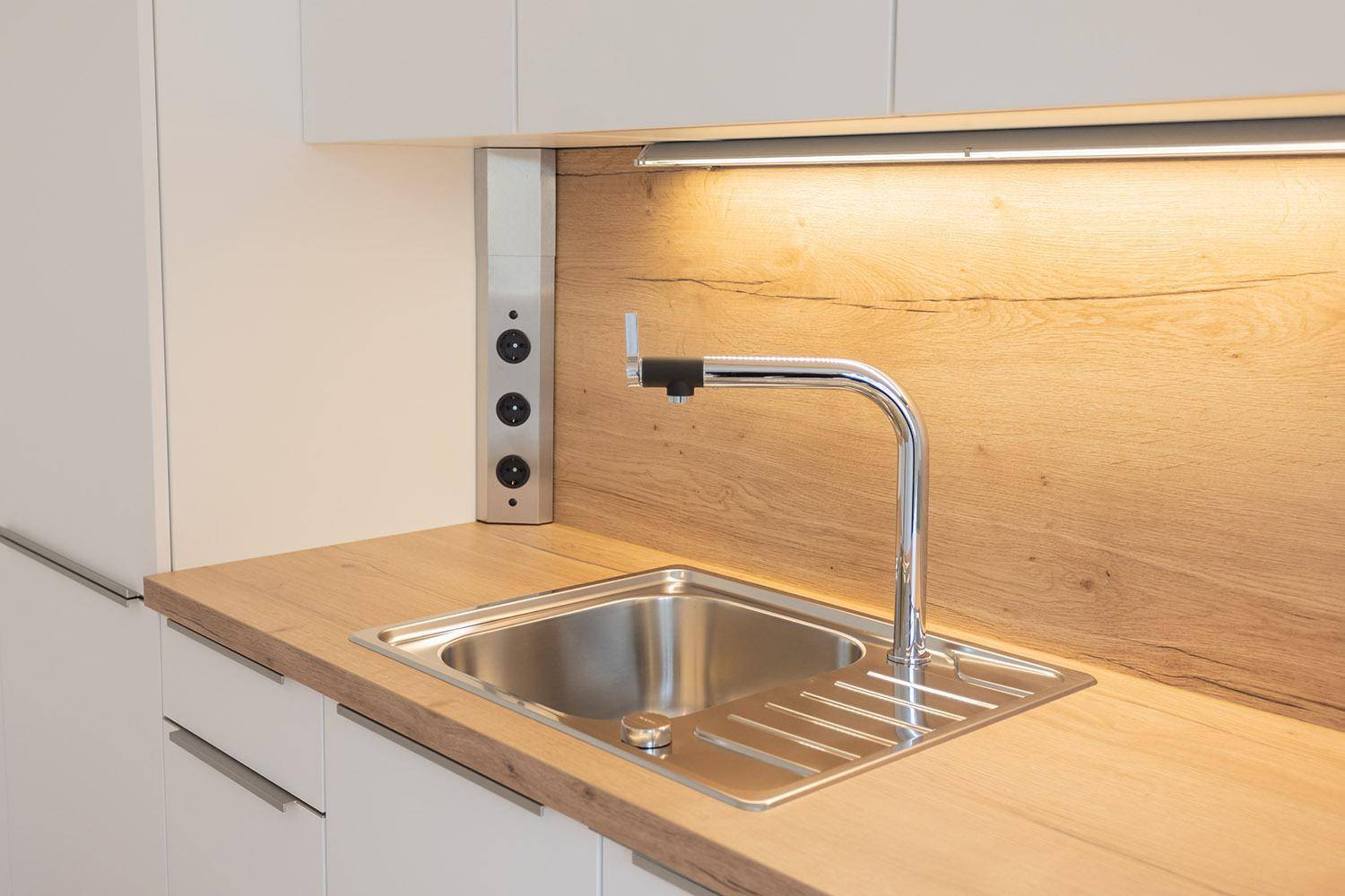 Moderne Küchenspüle mit Armatur und Holzarbeitsplatte, ergänzt durch praktische Steckdosenleiste.