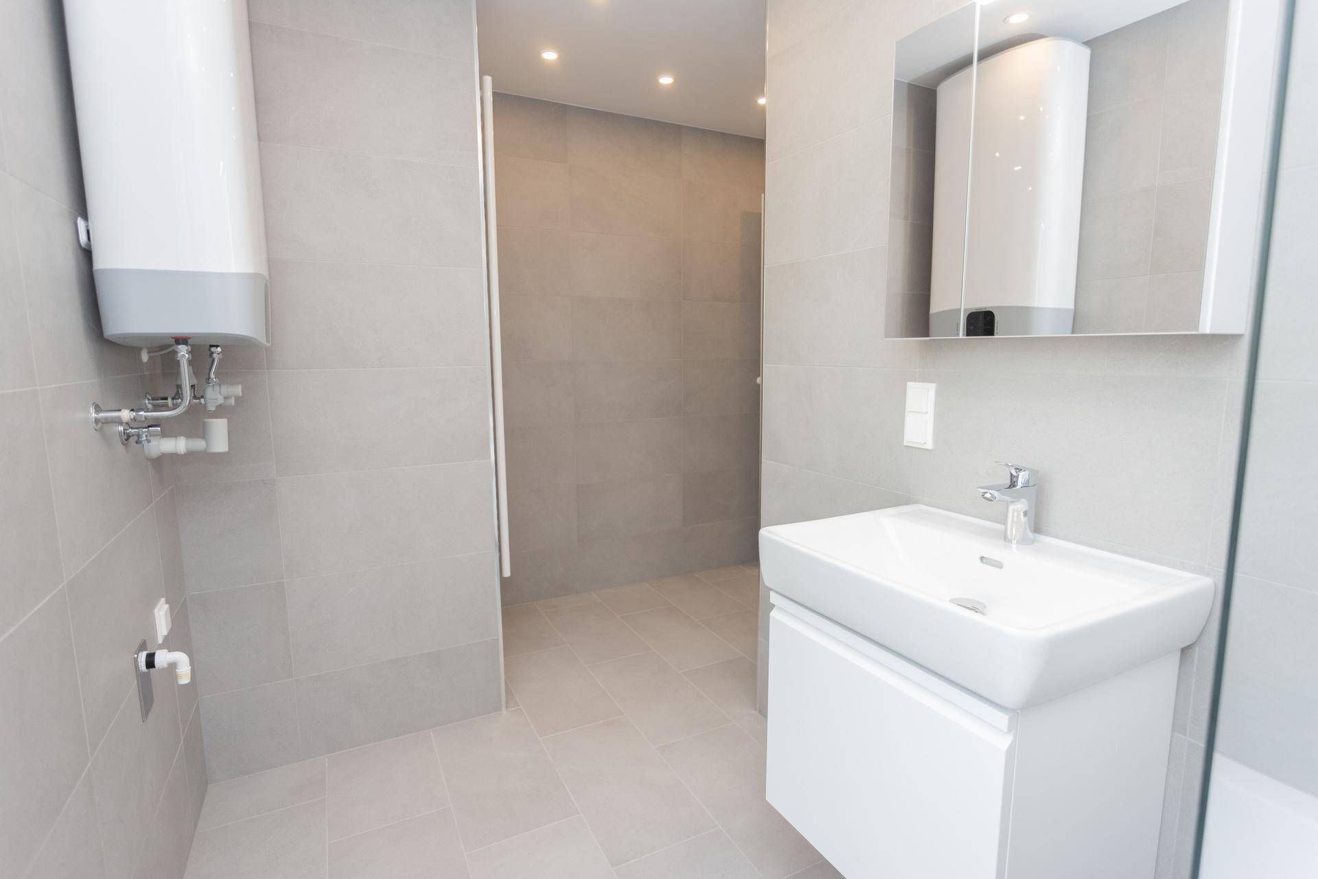 Modernes Badezimmer mit Waschtisch, Spiegelschrank und durchgängigen grauen Fliesen.