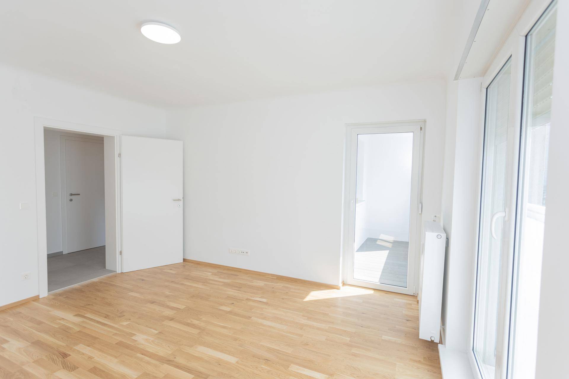 Helles Wohnzimmer mit Parkettboden und Zugang zu einem Balkon, ideal für Tageslicht.