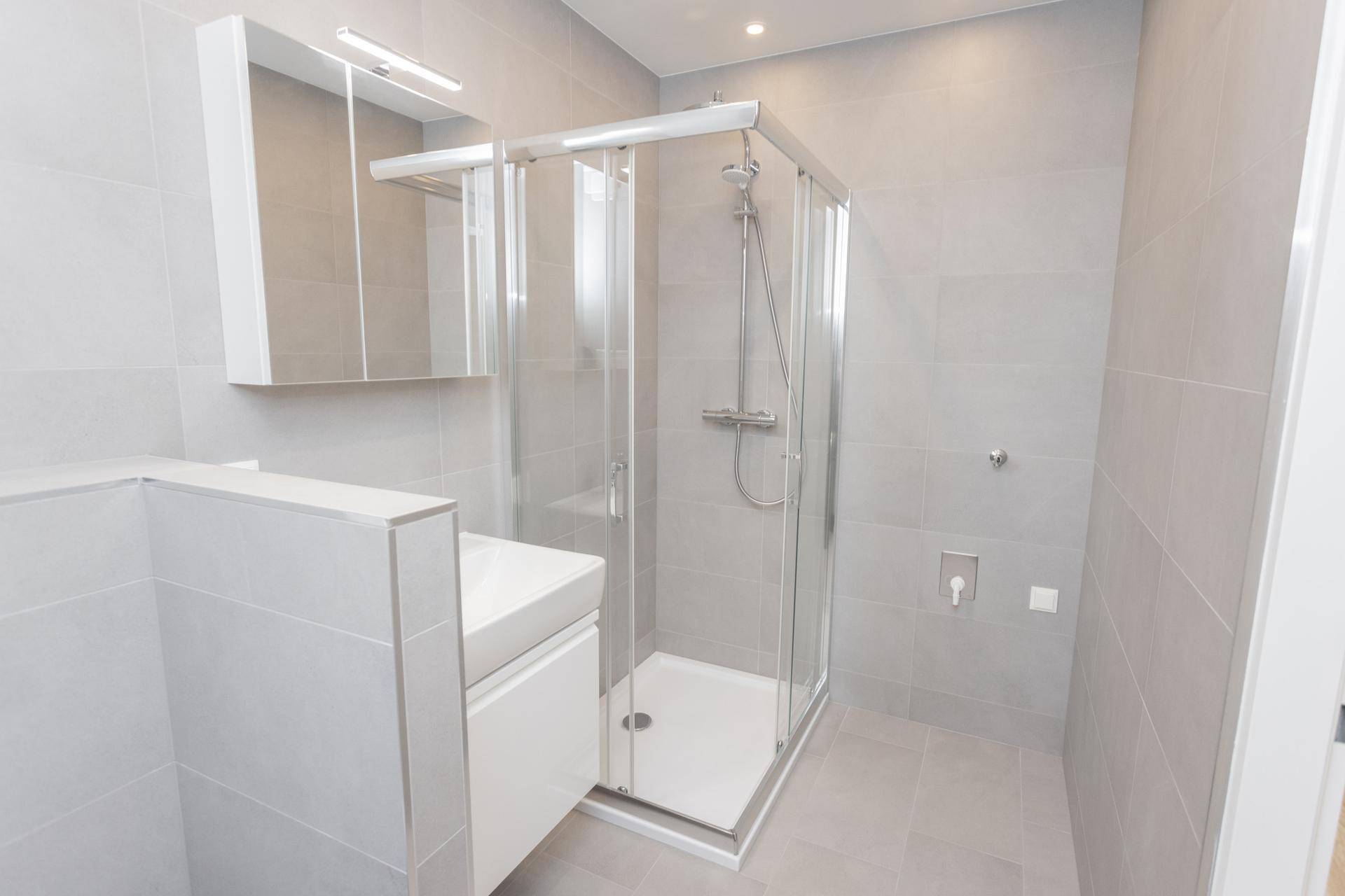Helles Badezimmer mit moderner Duschkabine, Waschbecken und Spiegelschrank, komplett gefliest.