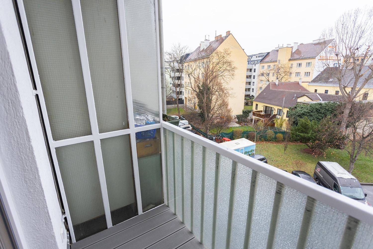 Balkon mit Blick auf die umliegenden Gebäude und einen grünen Innenhof mit Bäumen.