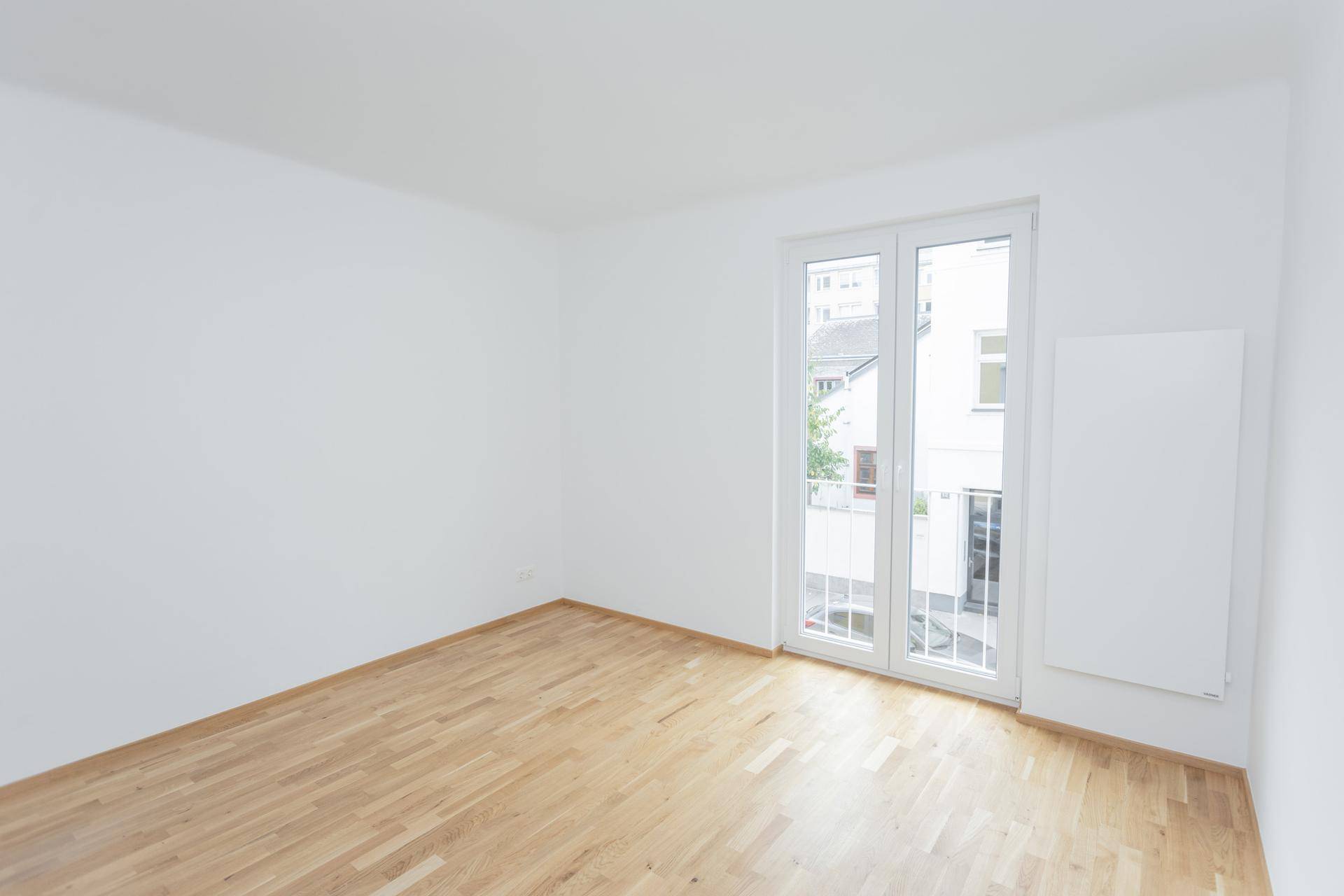 Heller, leerer Raum mit Holzboden und französischem Balkon, ideal als Schlafzimmer.