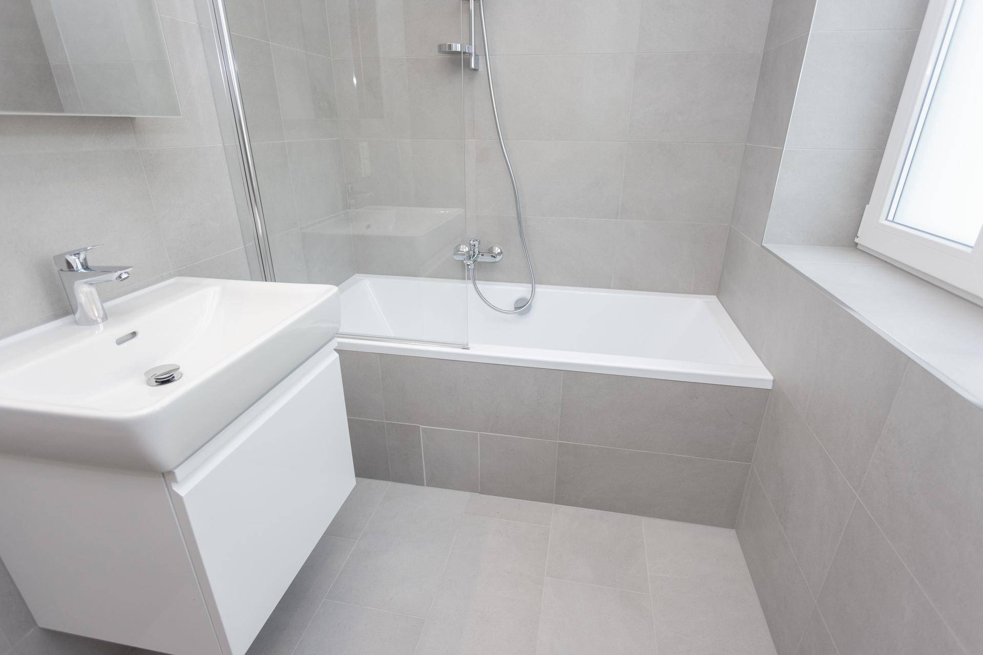 Helles Badezimmer mit Badewanne, Dusche, modernem Waschtisch und Fenster.