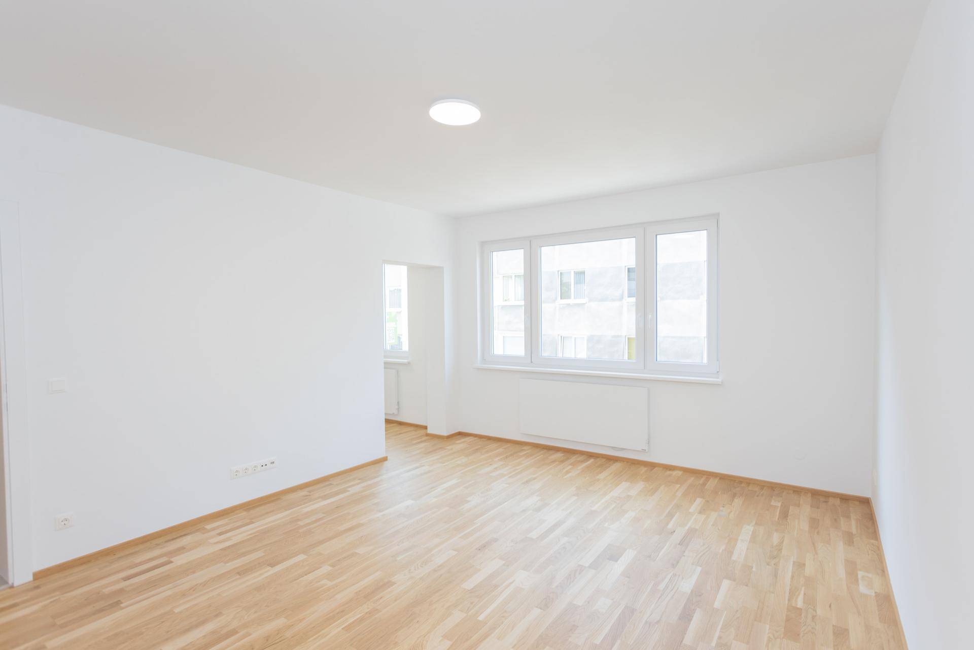 Heller und leerer Wohnraum mit Parkettboden und breiten Fenstern, bereit zur individuellen Gestaltung.