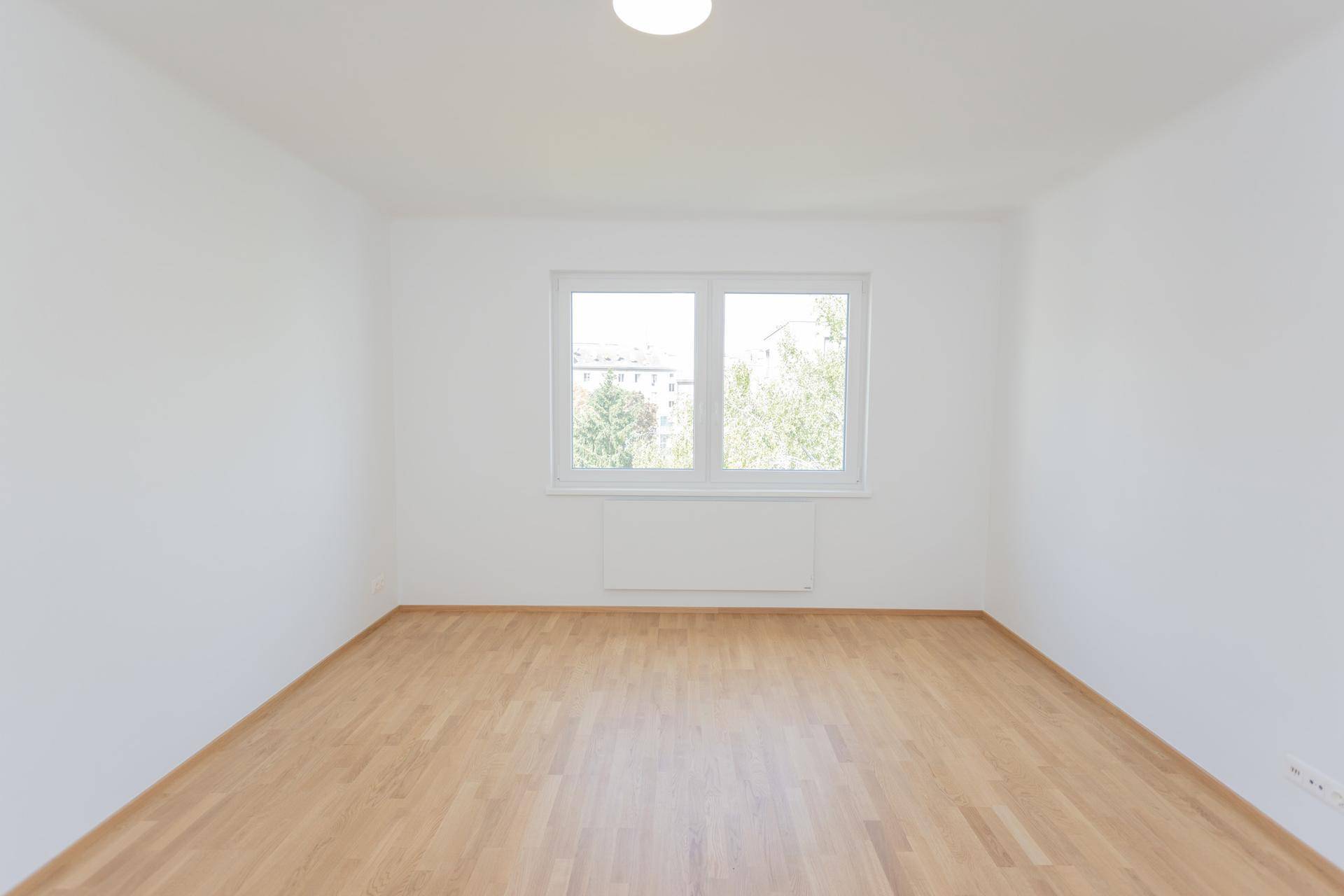 Geräumiges, leeres Zimmer mit großen Fenstern und hellem Parkettboden, ideal für Wohnzwecke.