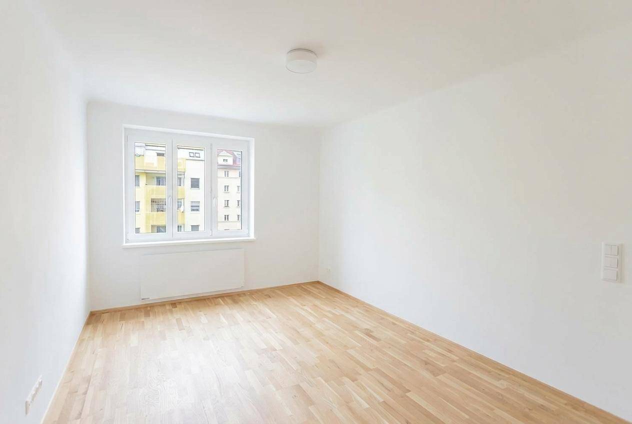 Geräumiger, leerer Raum mit Parkettboden und großen Fenstern, die viel Tageslicht hereinlassen.