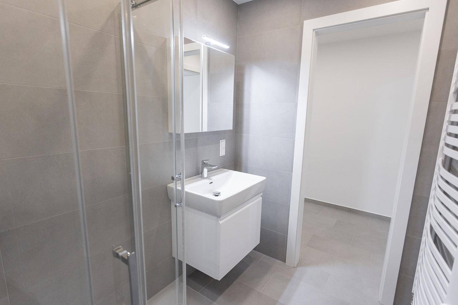 Helles Badezimmer mit modernem Waschtisch, Spiegelschrank und Zugang zum Flur.