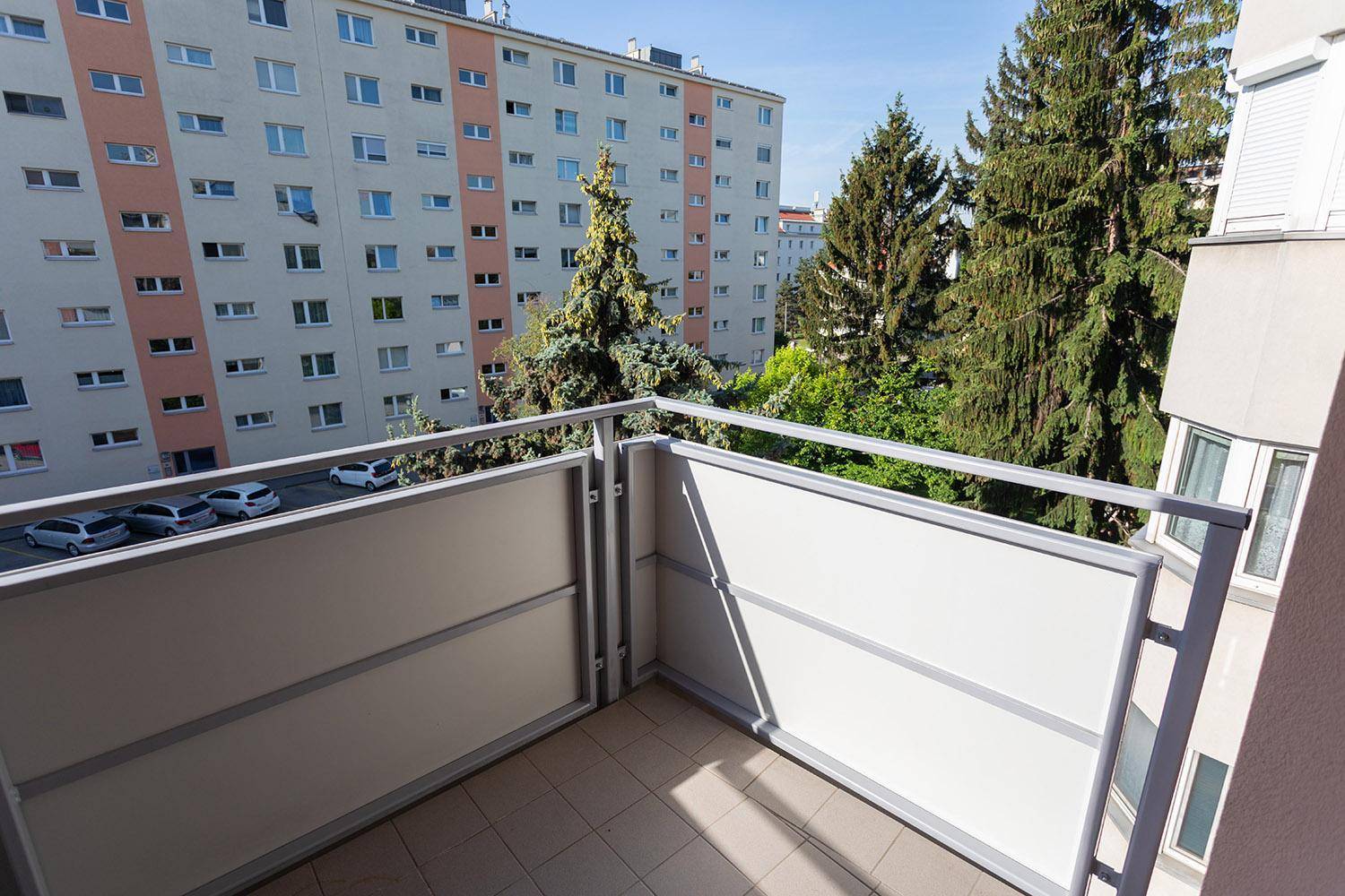Balkon mit Fliesenboden und grüner Aussicht auf Bäume und Wohngebäude.