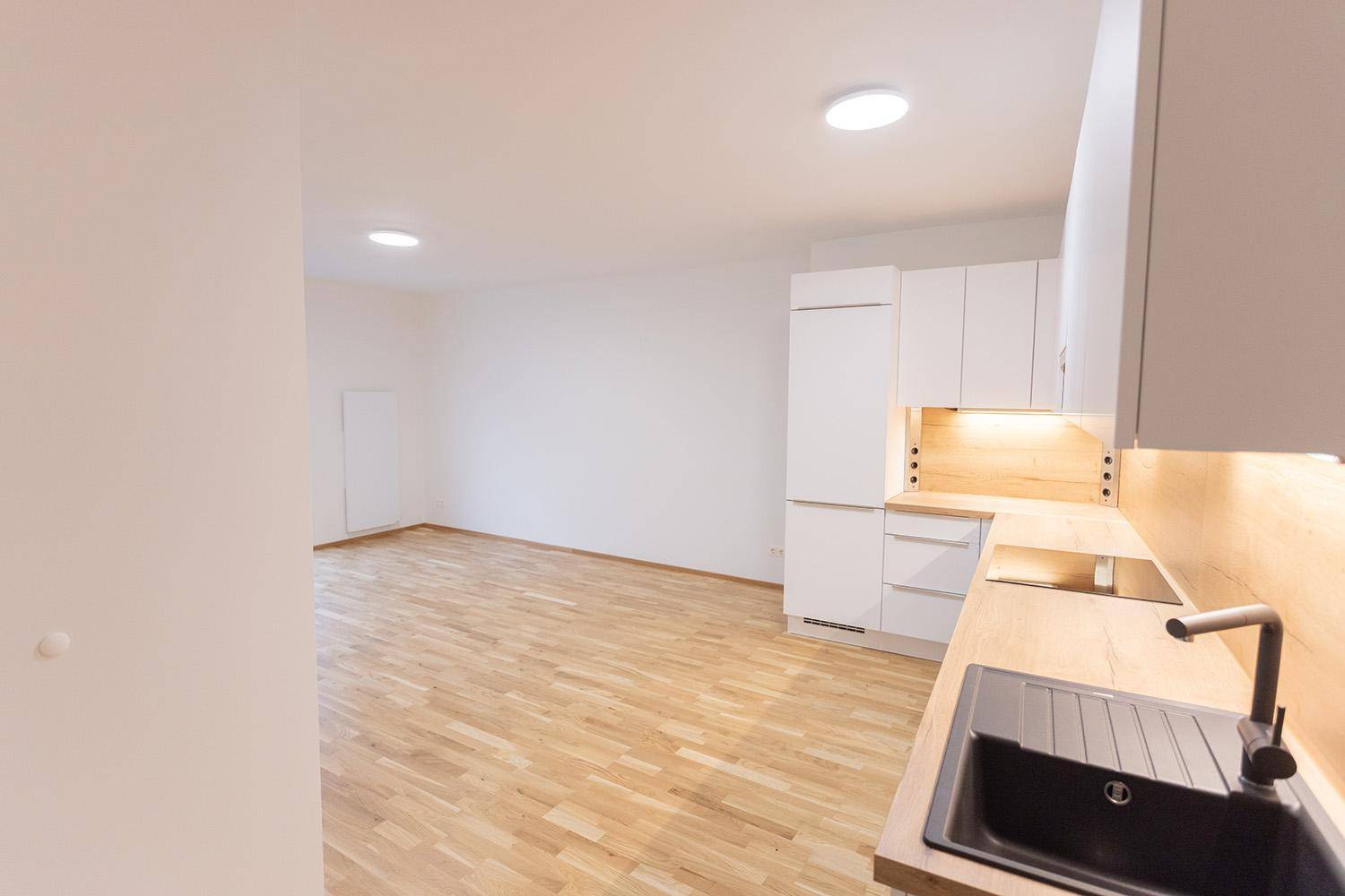 Moderne, offene Küche mit weißen Schränken, Holzarbeitsplatte und Blick in den Wohnbereich.