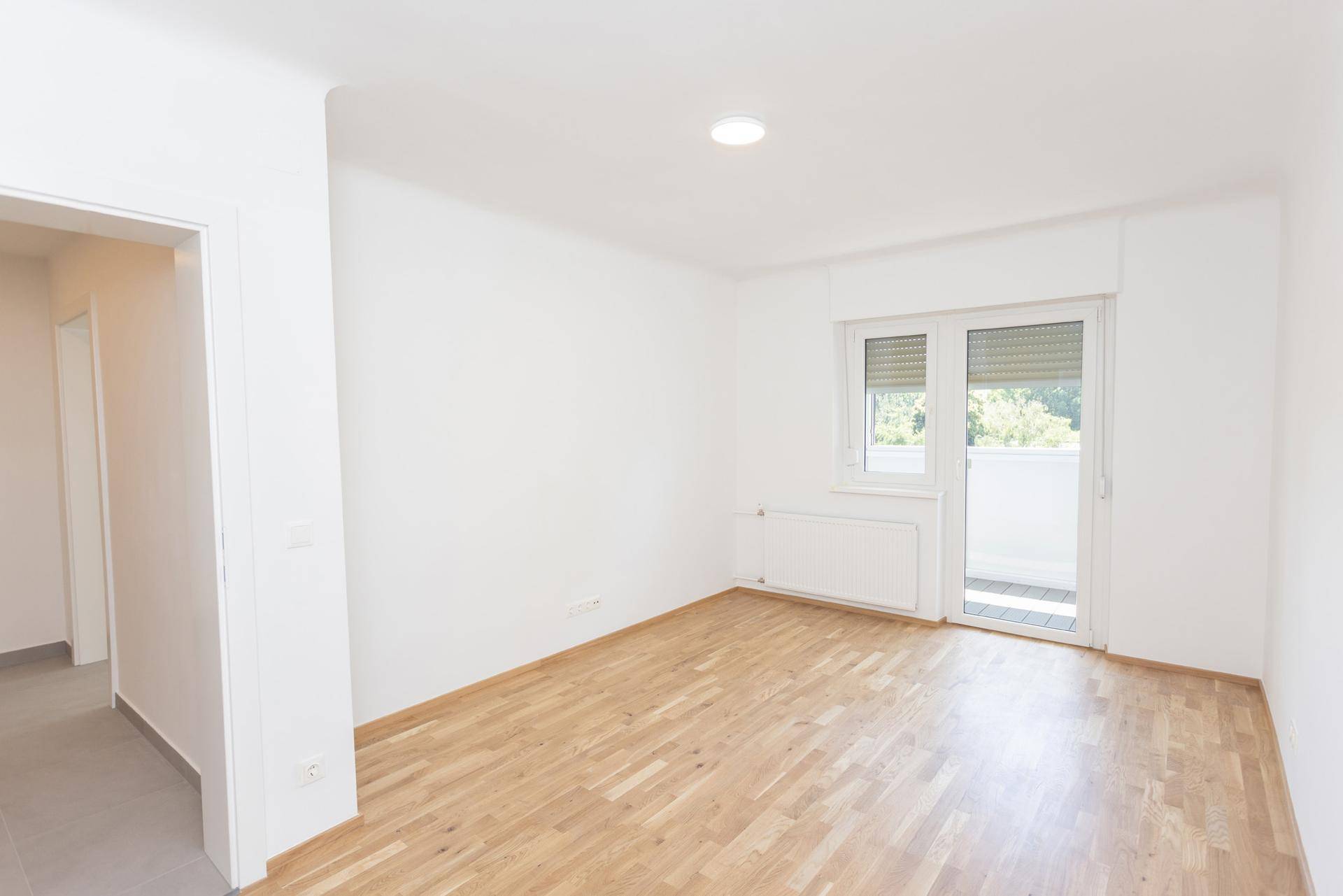 Heller Raum mit Holzboden und Zugang zu einem Balkon, ideal als Wohn- oder Schlafzimmer.