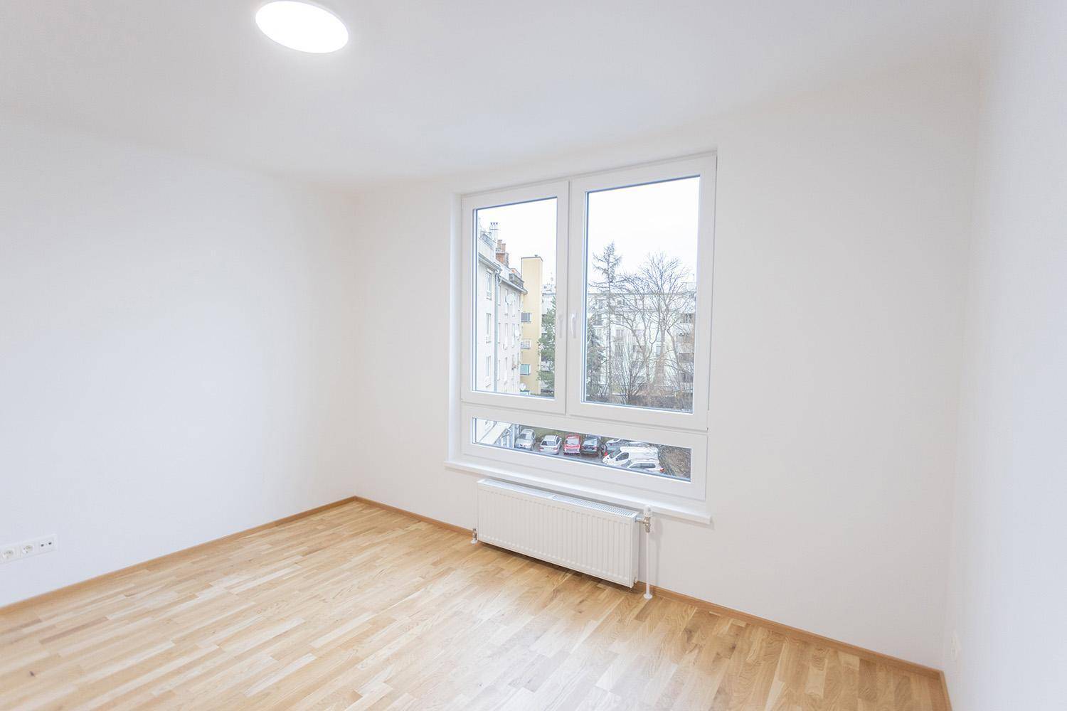 Helles Schlafzimmer mit Holzboden und großem Fenster, das viel Tageslicht hereinlässt.