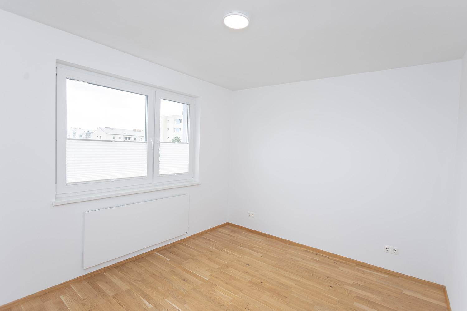 Helles Schlafzimmer mit Eichenparkett und großem Fenster, bietet viel Tageslicht.