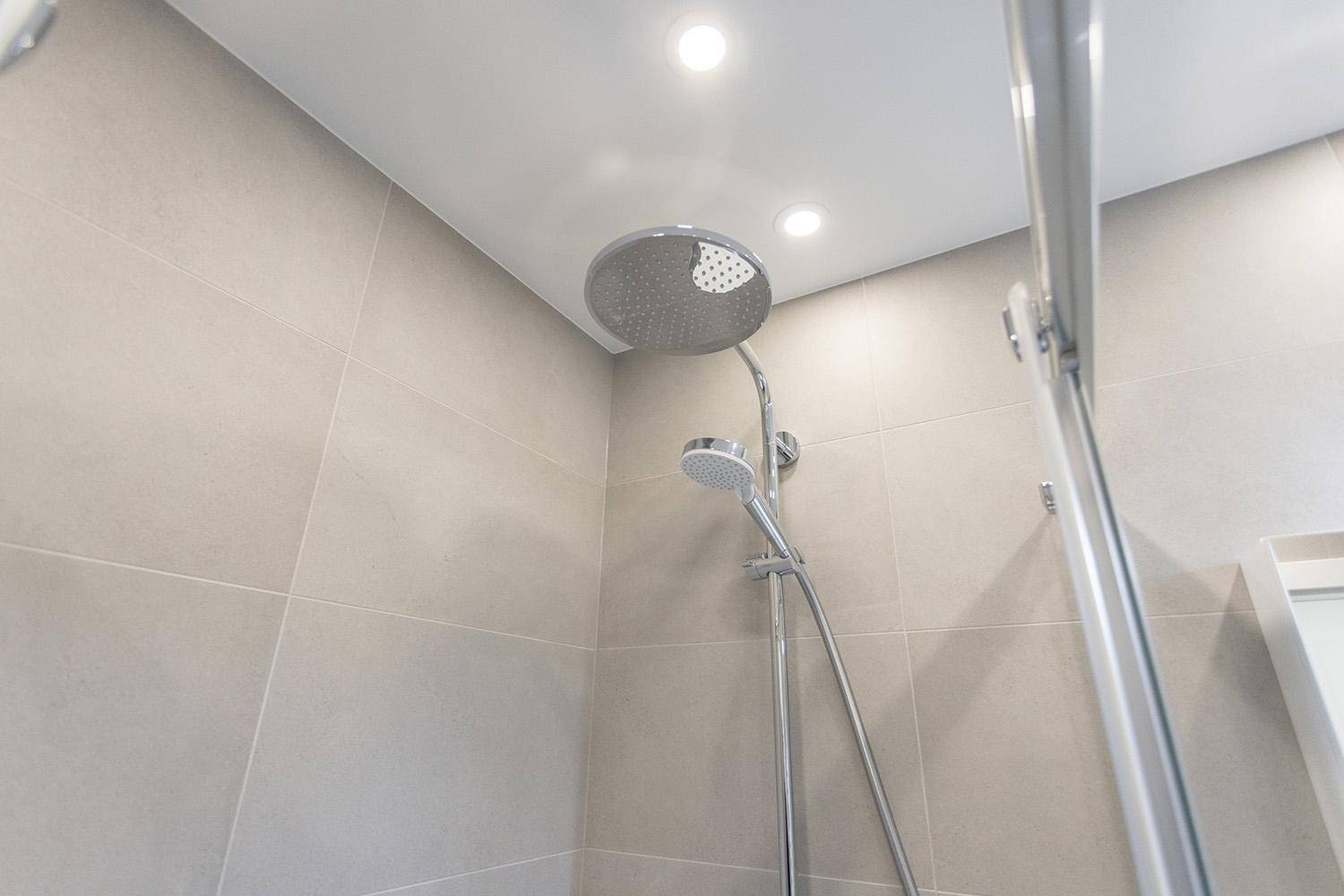 Nahaufnahme einer modernen Regendusche in einem gefliesten Badezimmer mit Einbaustrahlern.