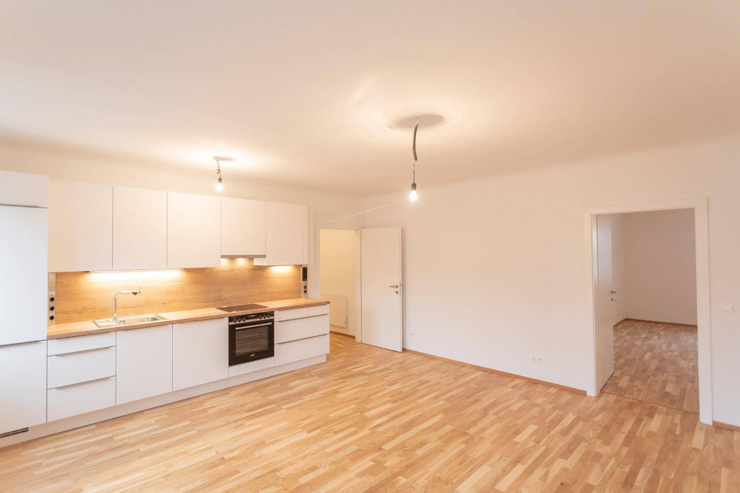 Moderne Einbauküche mit weißen Schränken und Holzarbeitsplatte, angrenzend an weiteren Raum.