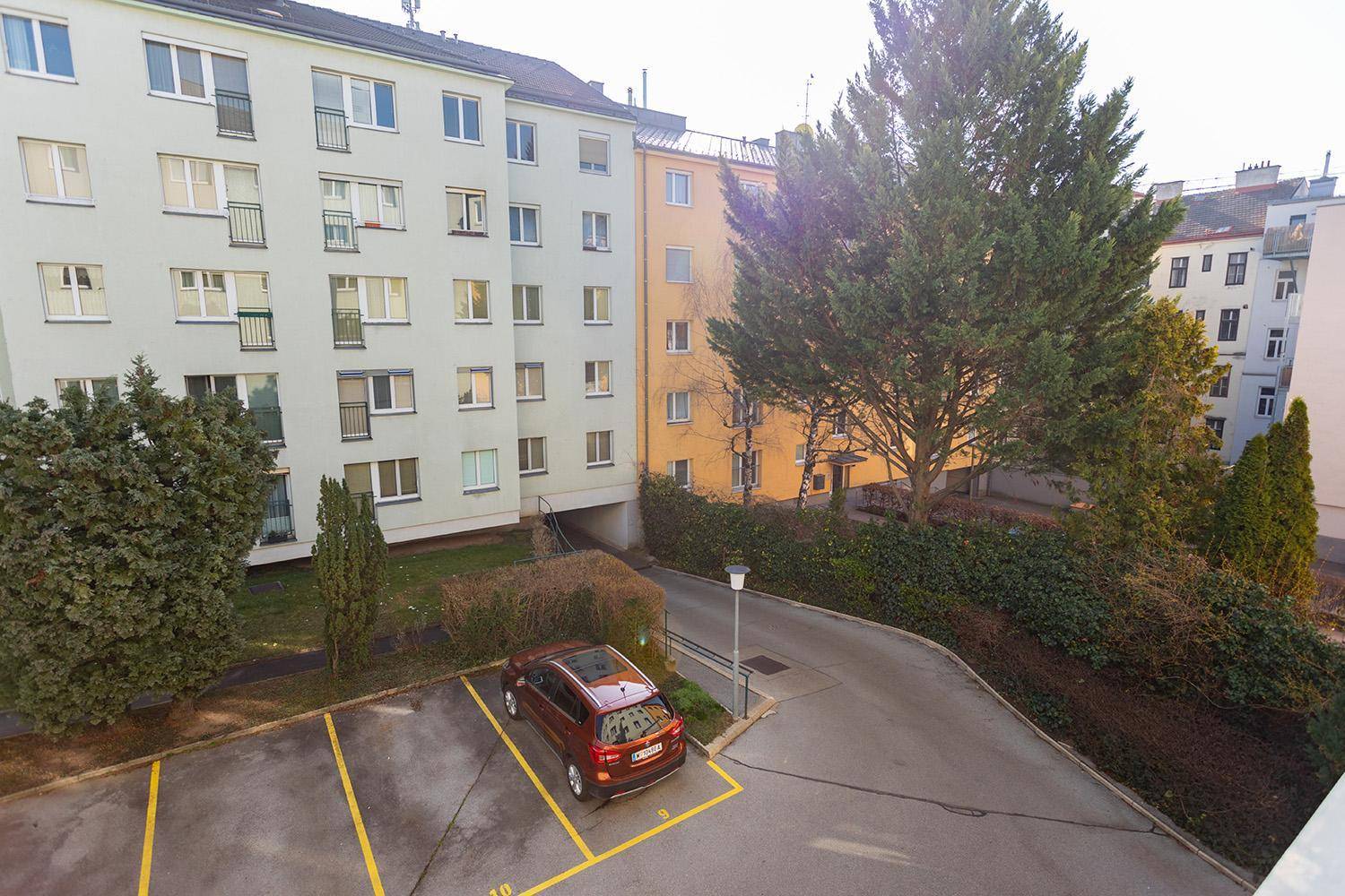 Außenansicht eines Mehrfamilienhauses mit Parkplätzen und grüner Umgebung.