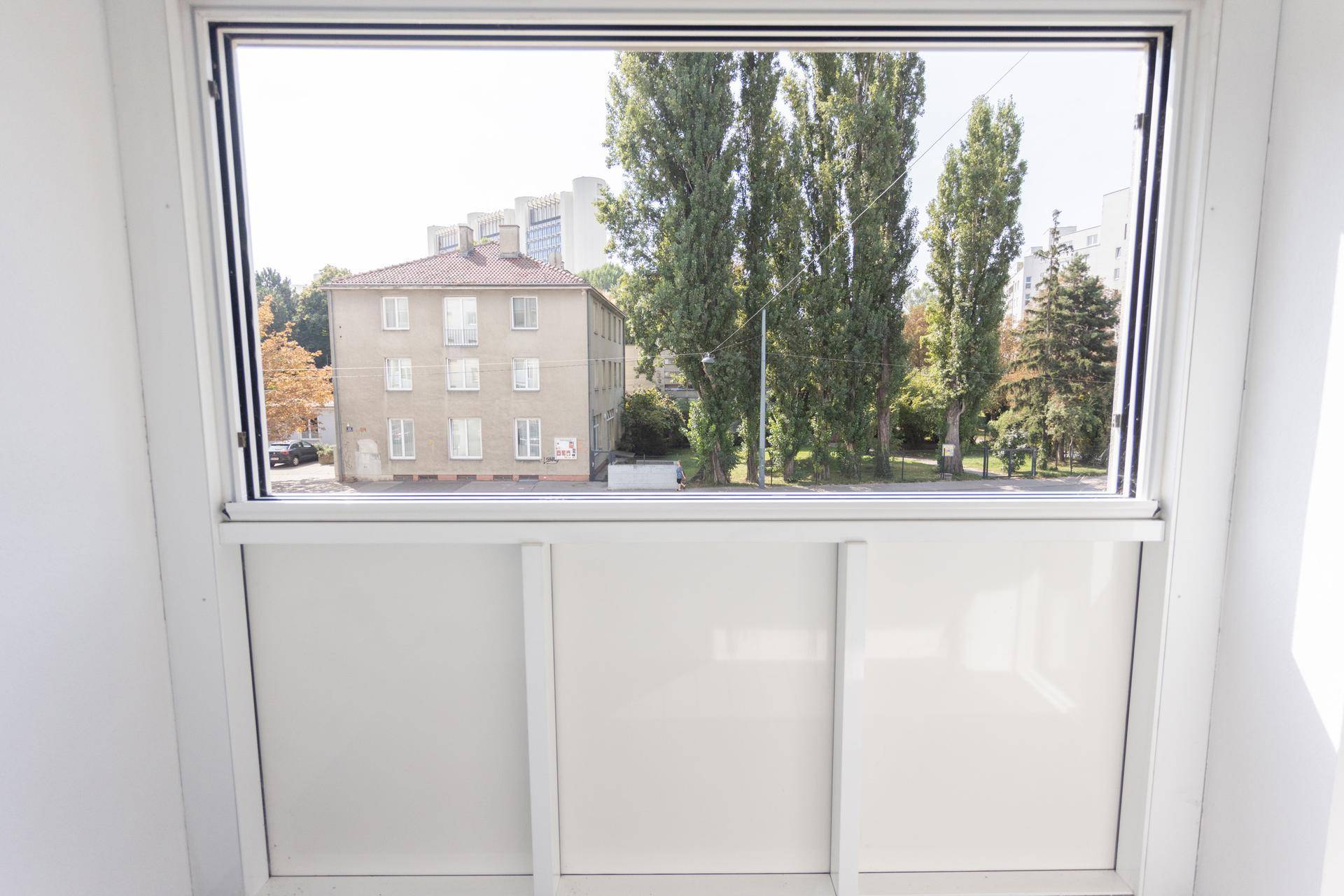 Heller Balkon mit Holzdielenboden und weitem Blick auf die Stadt und grüne Bäume.