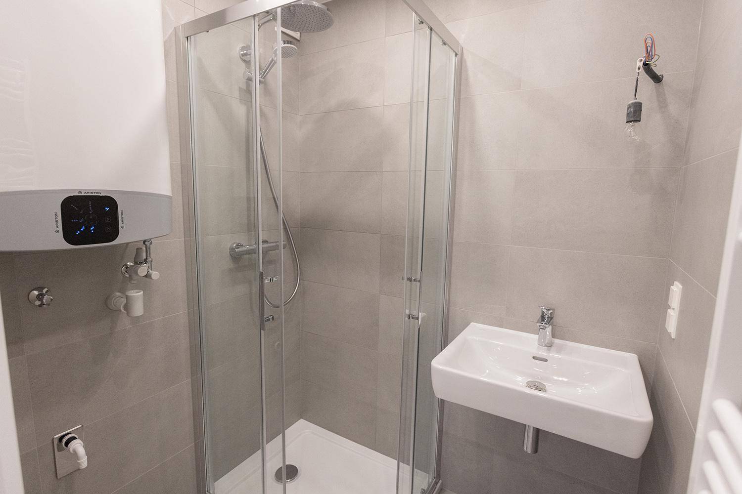 Modernes Badezimmer mit Duschkabine, Waschbecken und Warmwasserboiler, komplett gefliest.