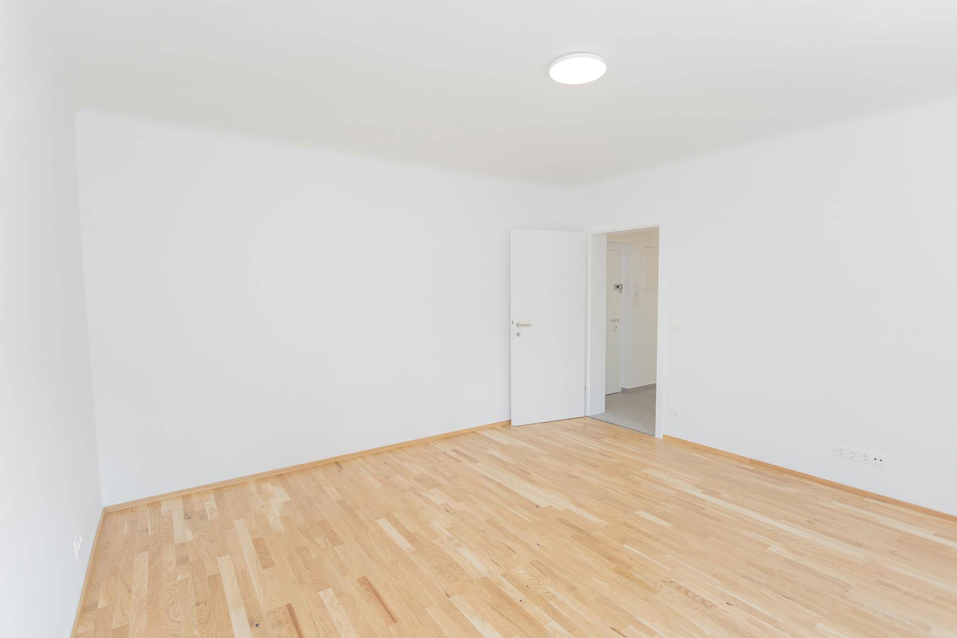 Leeres, helles Schlafzimmer mit Holzboden und offener Tür, bereit zur individuellen Gestaltung.