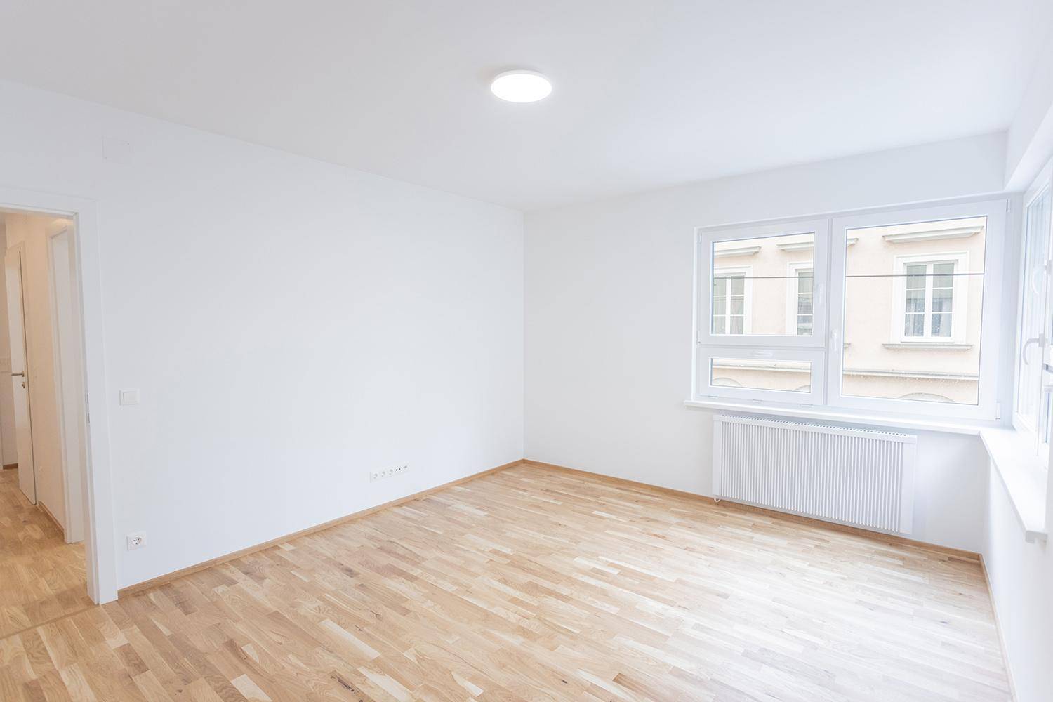 Helles Schlafzimmer mit Holzparkettboden und großen Fenstern, das viel Tageslicht hereinlässt.