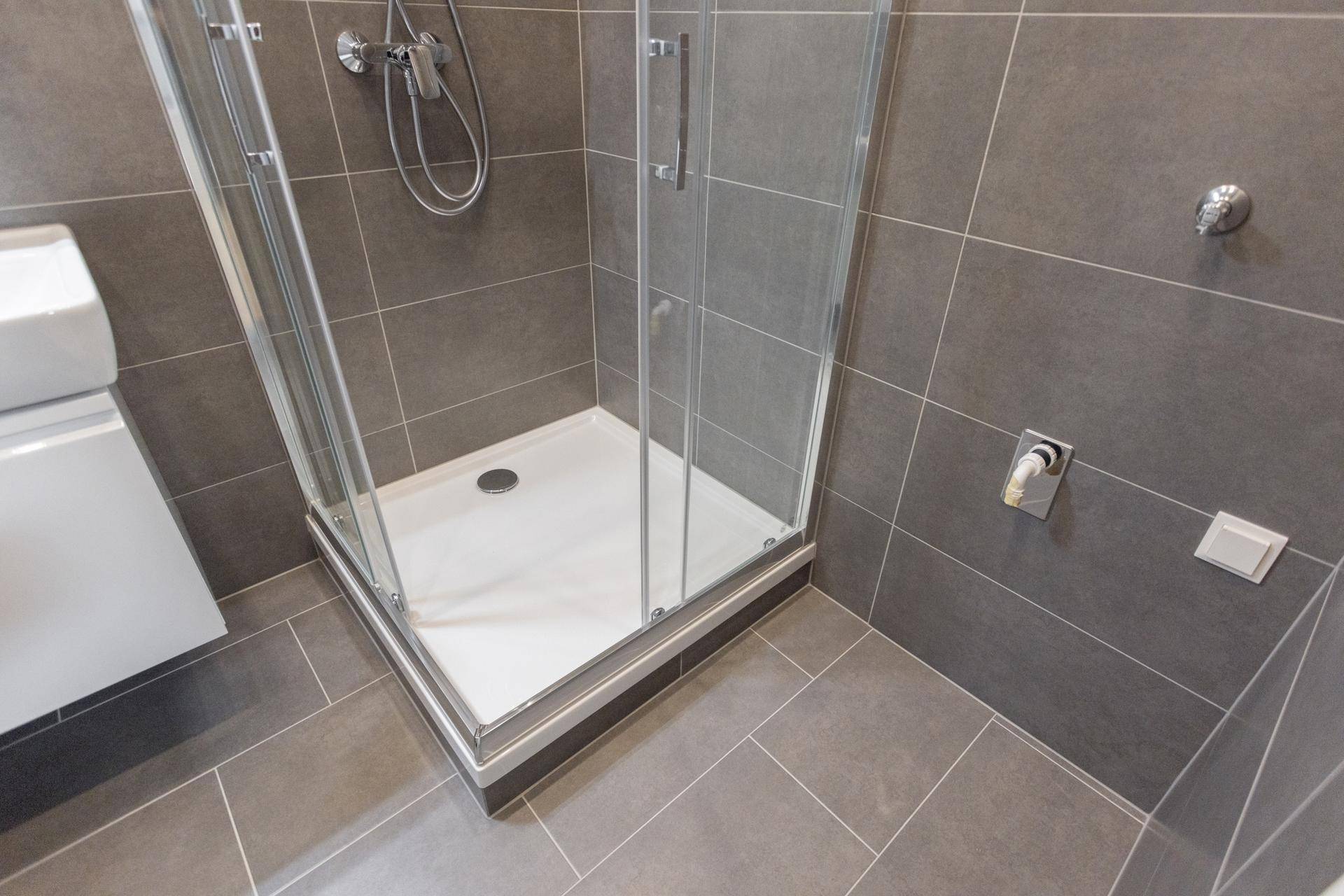 Duschkabine mit Glaswänden und modernen grauen Fliesen im Badezimmer.