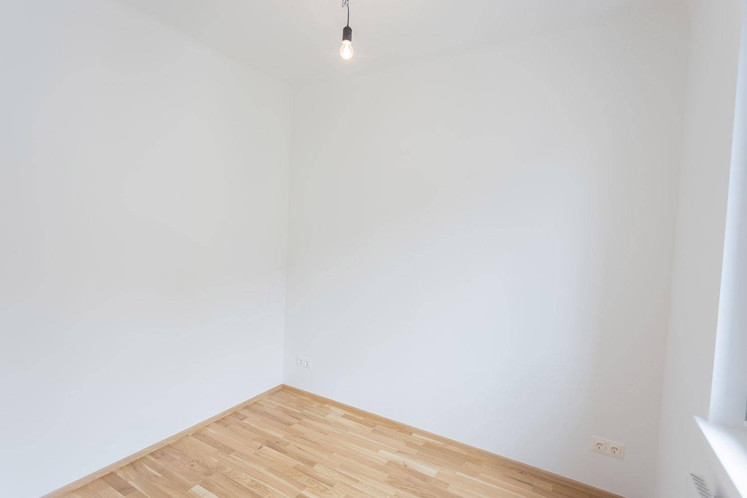 Helles, leeres Schlafzimmer mit Holzboden und weiß gestrichenen Wänden, bereit zur individuellen Gestaltung.