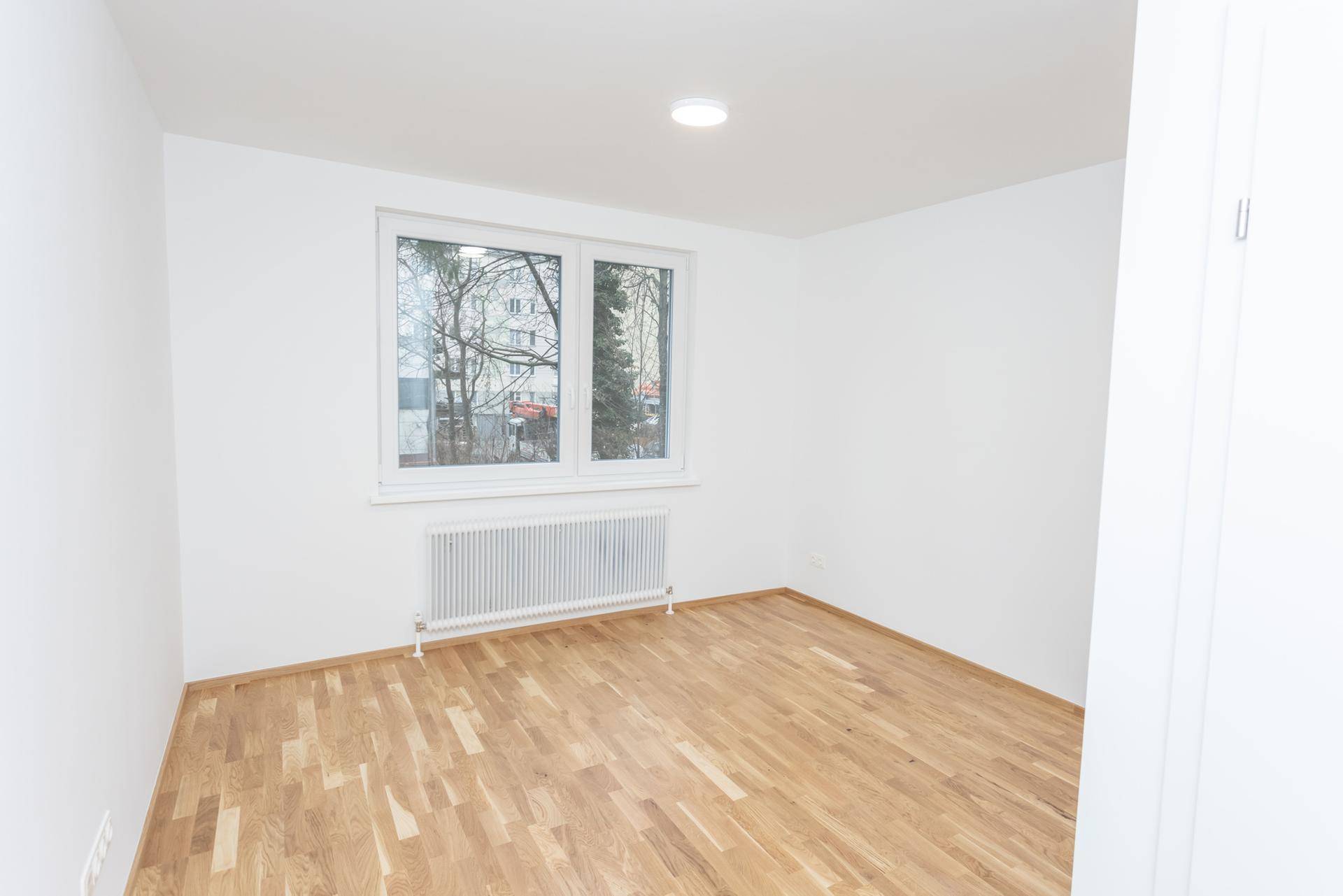Heller, leerer Raum mit Parkettboden und großem Fenster.