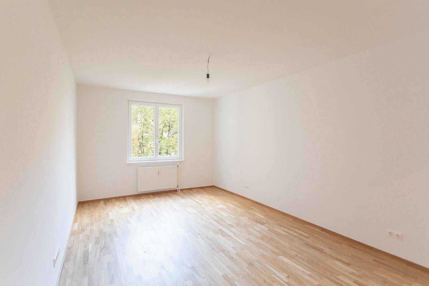 Helles, leeres Zimmer mit Holzboden und Fenster, das viel Tageslicht bietet.