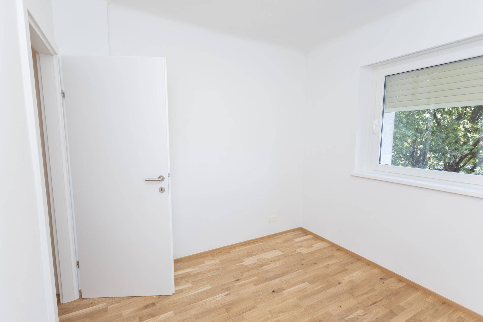 Helles, leeres Zimmer mit Holzboden und Fenster, bereit zur individuellen Gestaltung.