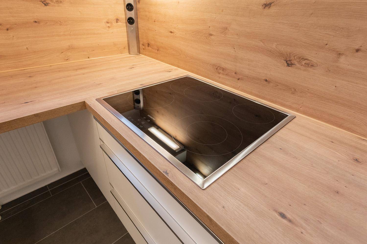 Nahaufnahme eines modernen Induktionskochfeldes, elegant in eine Holzarbeitsplatte integriert.