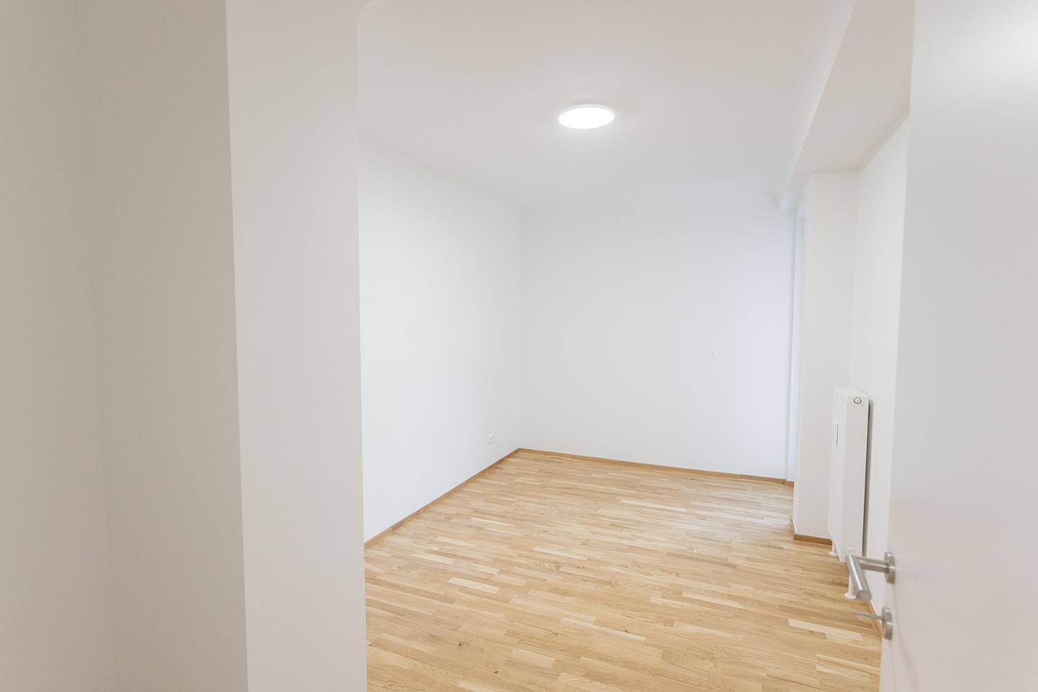 Heller, leerer Raum mit Parkettboden und weiß gestrichenen Wänden, ideal für verschiedene Nutzungen.