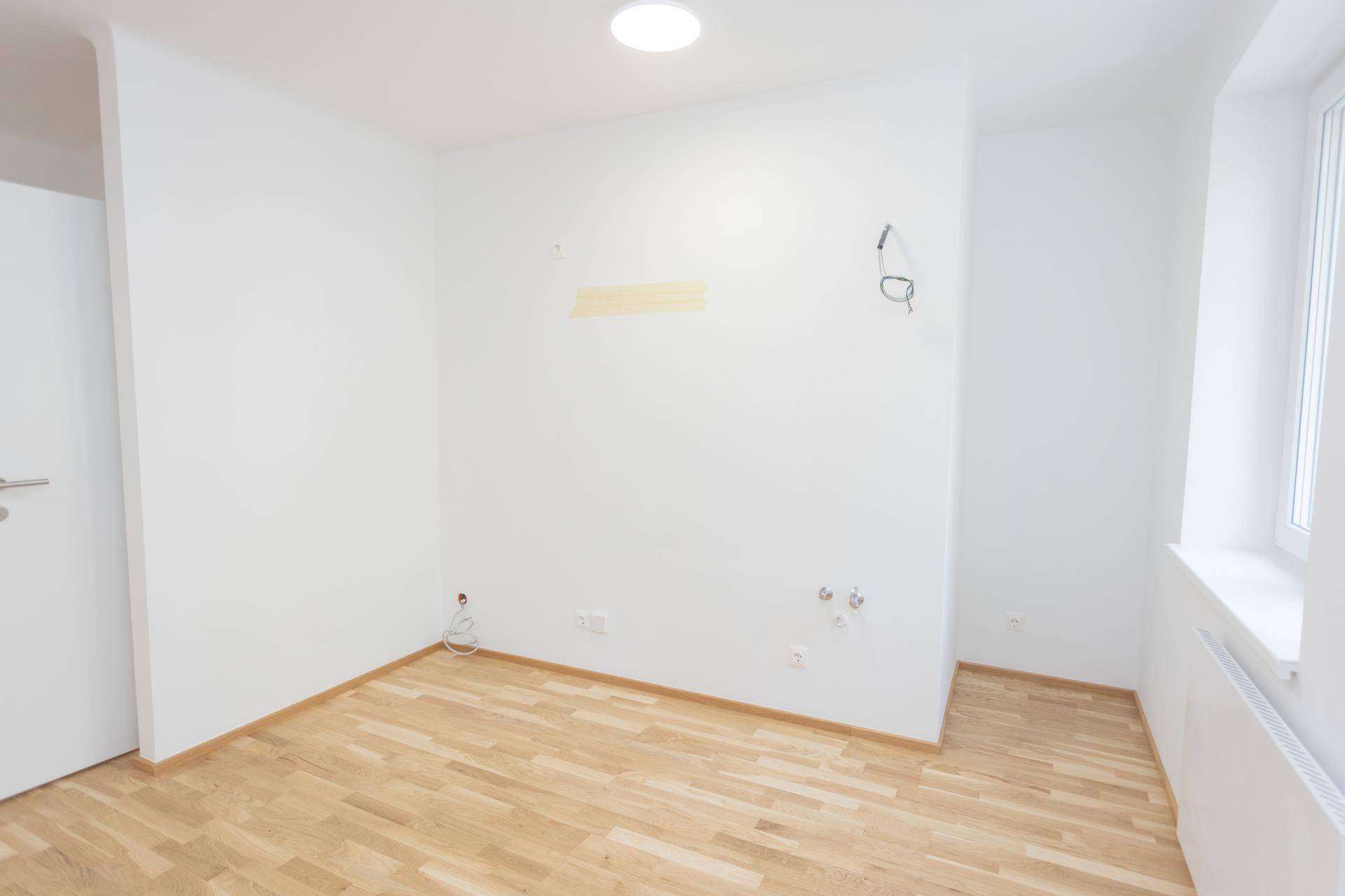 Vorbereiteter Küchenbereich mit Parkettboden und Anschlüssen für die Kücheninstallation.