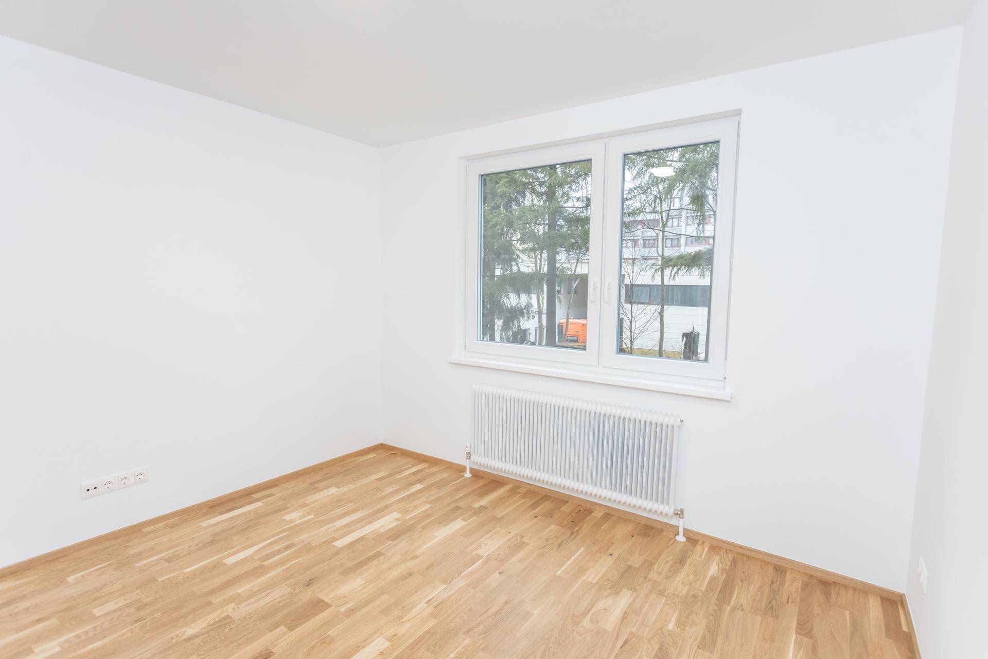 Heller, leerer Raum mit Parkettboden und Fenster mit Blick ins Grüne.