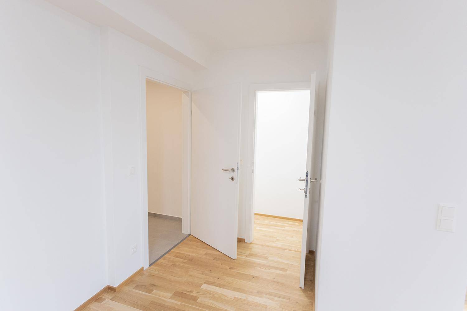Heller Raum mit Holzboden und offenen Türen, die zu weiteren Zimmern führen.