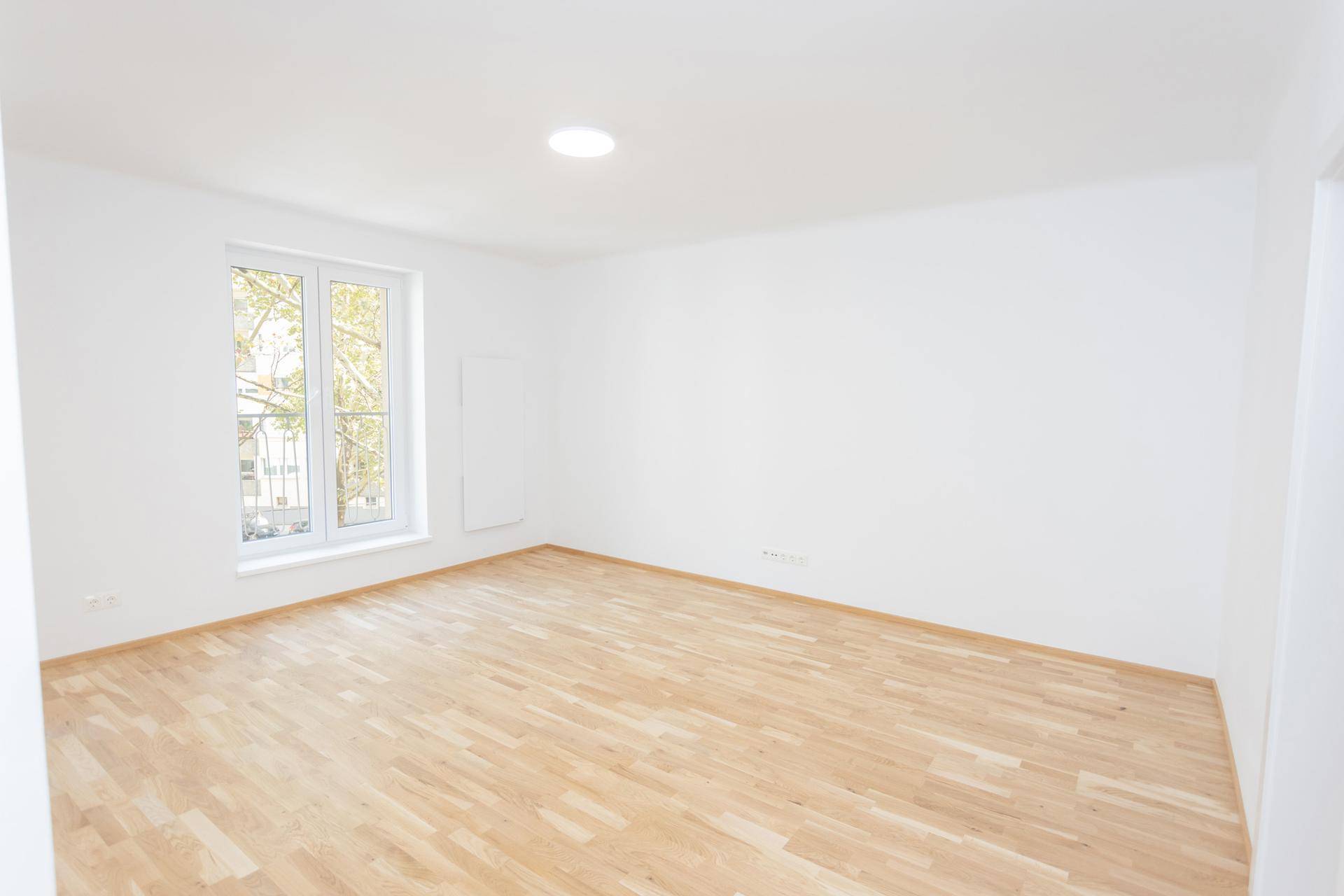 Geräumiges Wohnzimmer mit hellem Parkettboden und viel Tageslicht durch das Fenster.