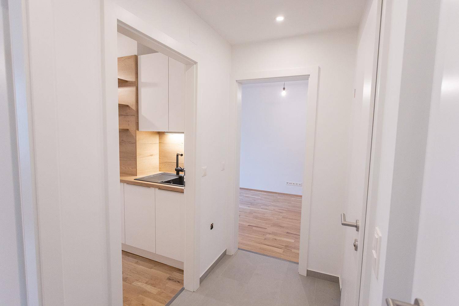 Flur mit Blick auf eine kompakte Küchenzeile und einen angrenzenden Raum mit Holzfußboden.