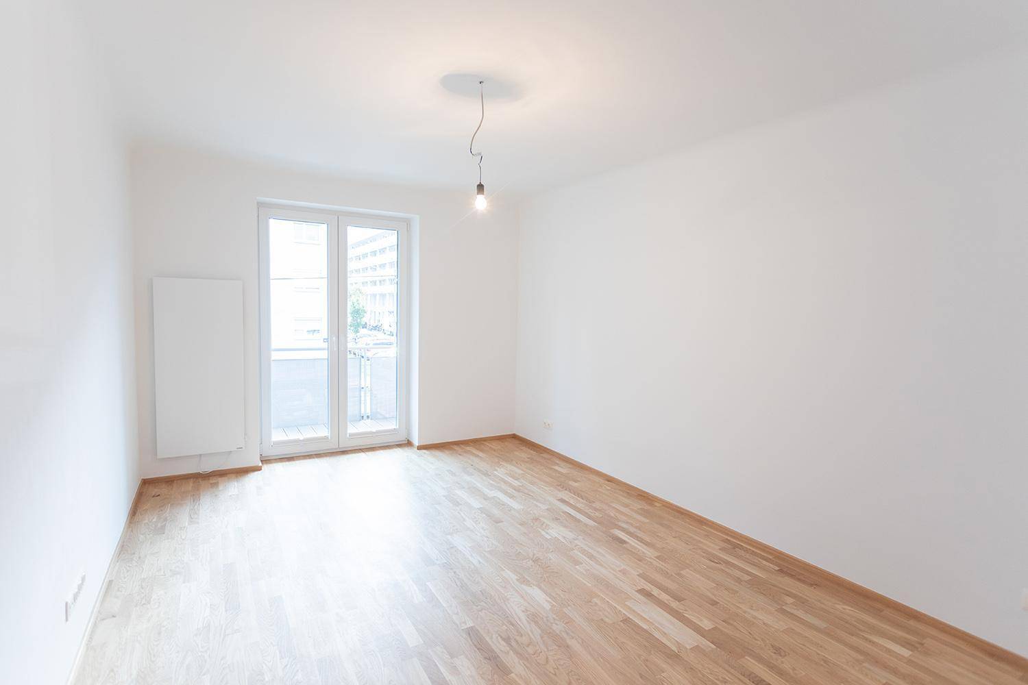 Helles, leeres Zimmer mit Parkettboden und direktem Zugang zum Balkon.