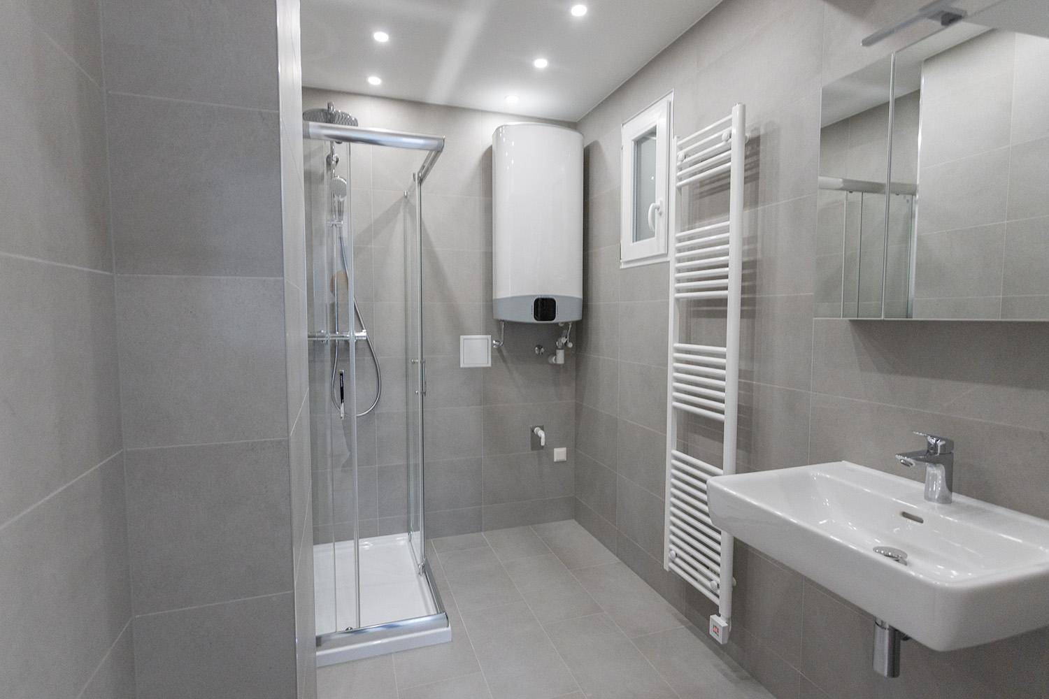 Modernes Badezimmer mit grauen Fliesen, Duschkabine, Waschbecken und beheiztem Handtuchhalter.