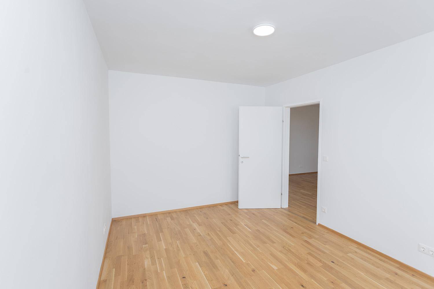 Leeres Schlafzimmer mit Eichenparkett und weiß gestrichenen Wänden, schlicht und hell.