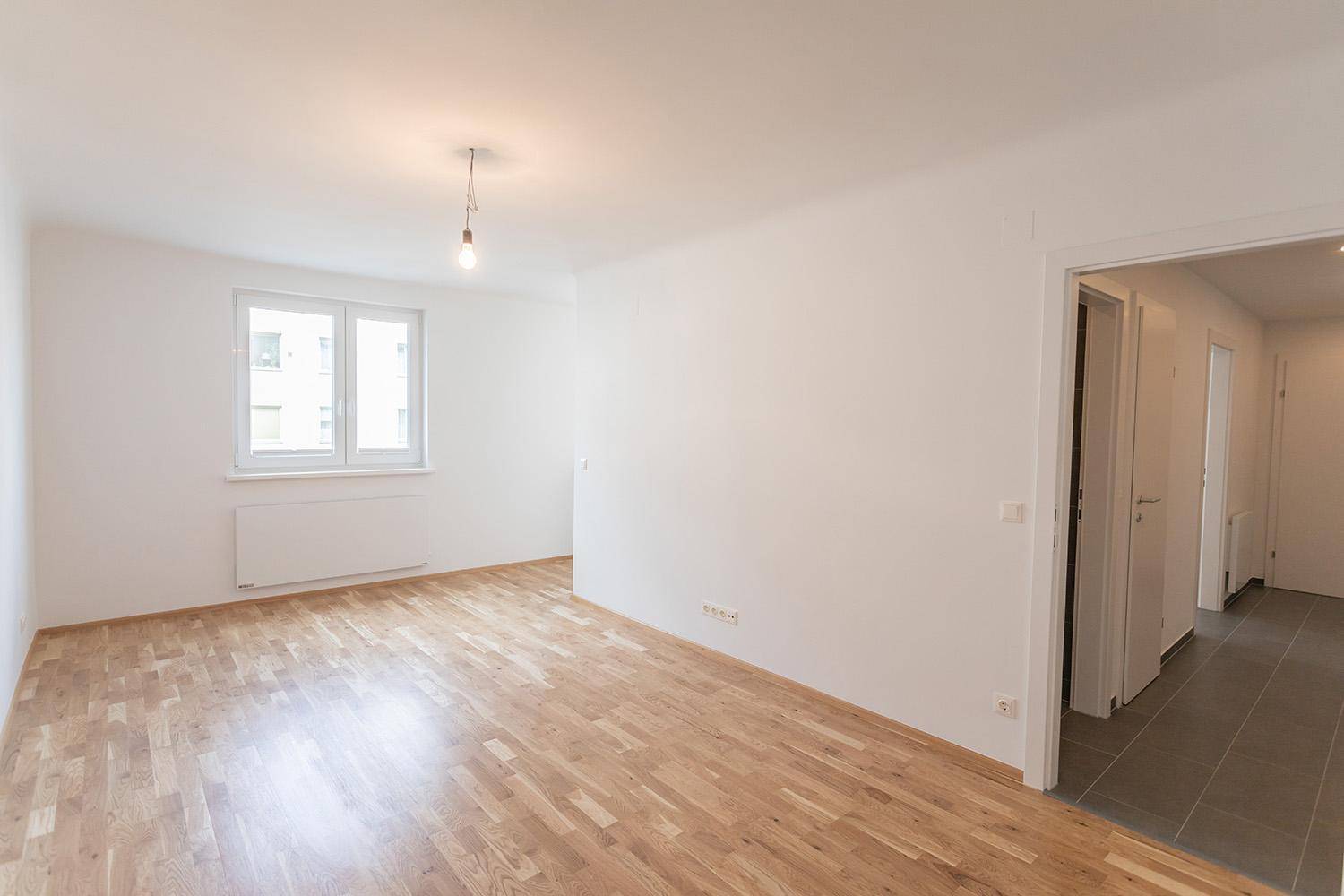 Heller Wohnraum mit Parkettboden und großem Fenster, bereit zur individuellen Einrichtung.