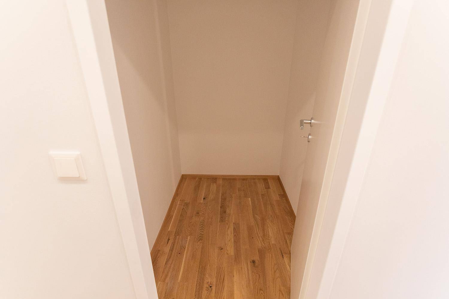 Kleiner, leerer Abstellraum mit hellem Holzfußboden und weißen Wänden.